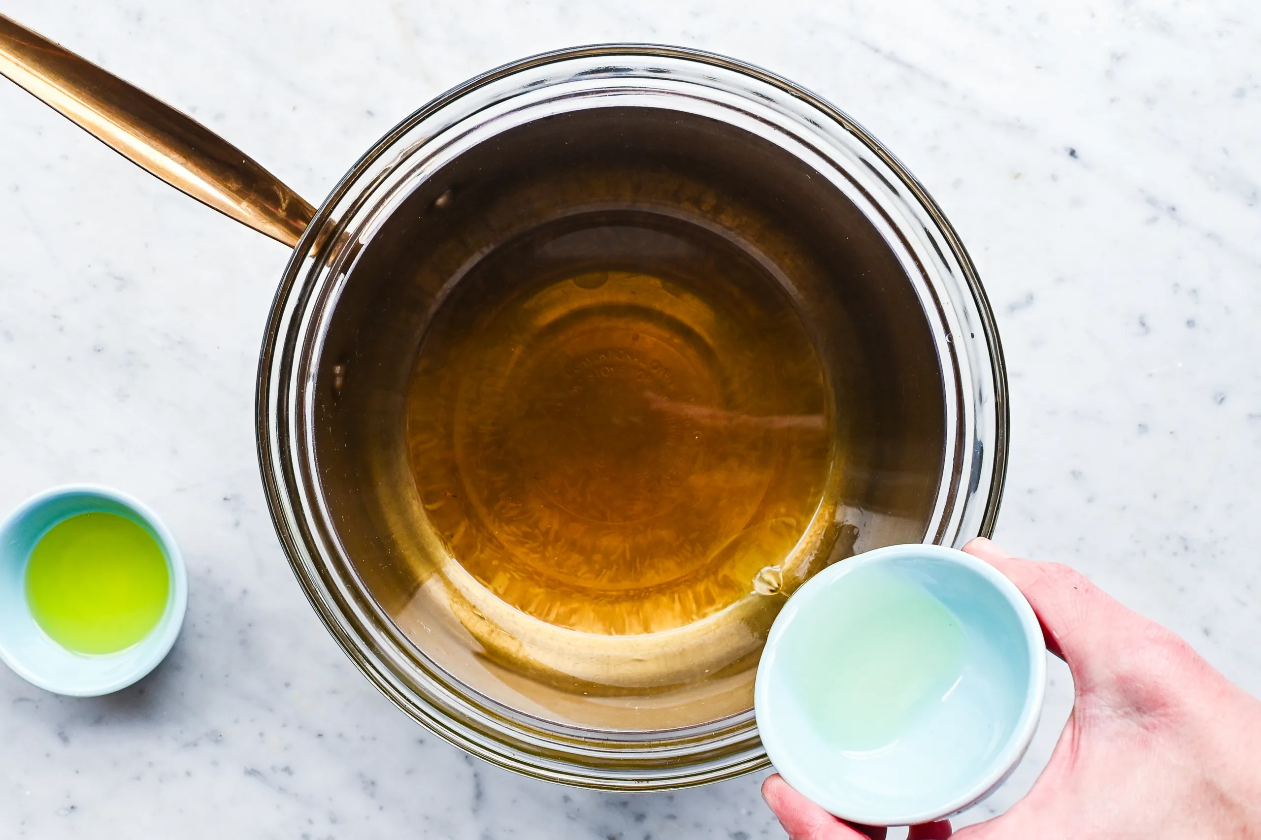 Melted beeswax and tallow mixture in a bowl during the process of making homemade hair pomade.