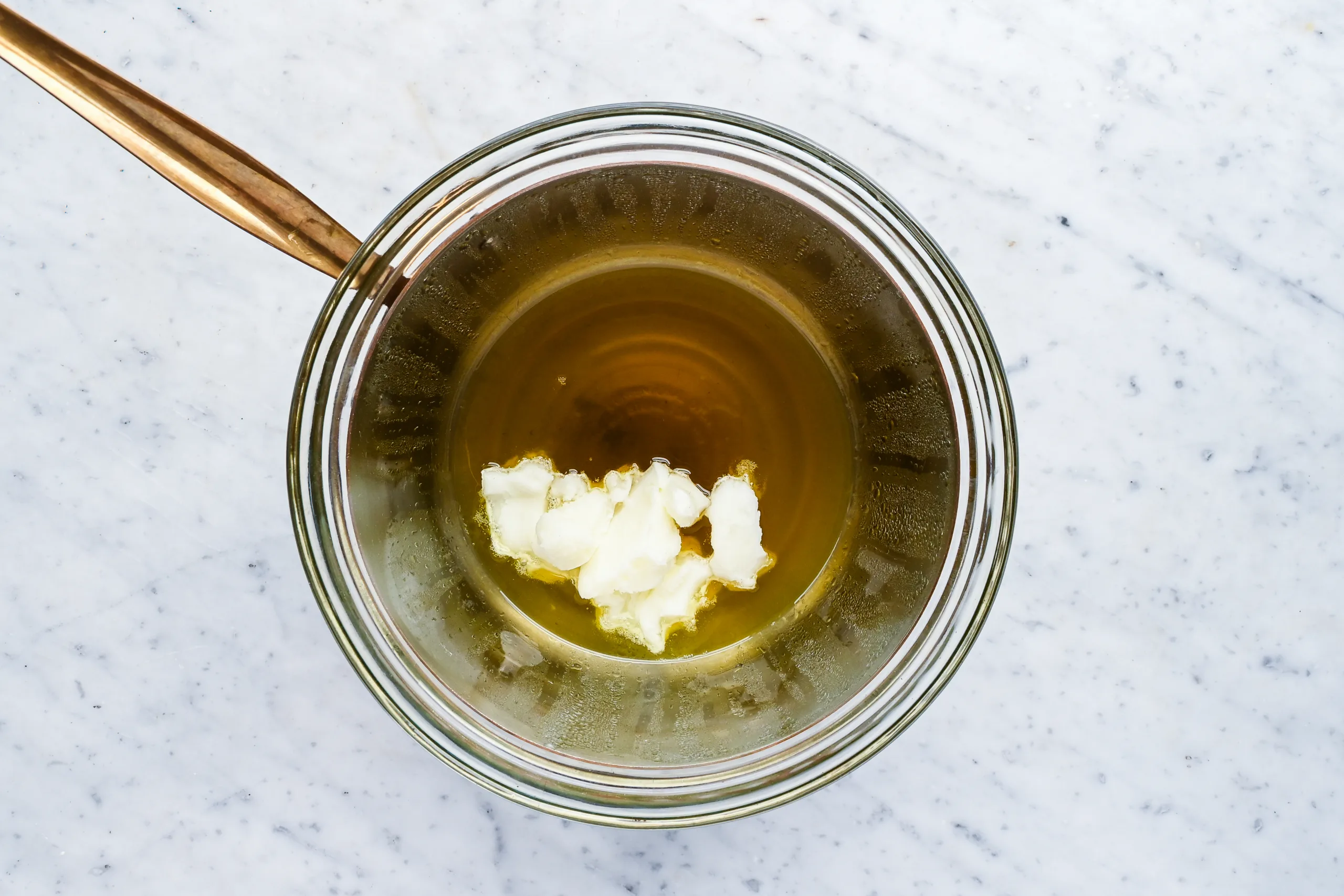 Beef tallow melting in a glass bowl over a double boiler for homemade natural pomade.