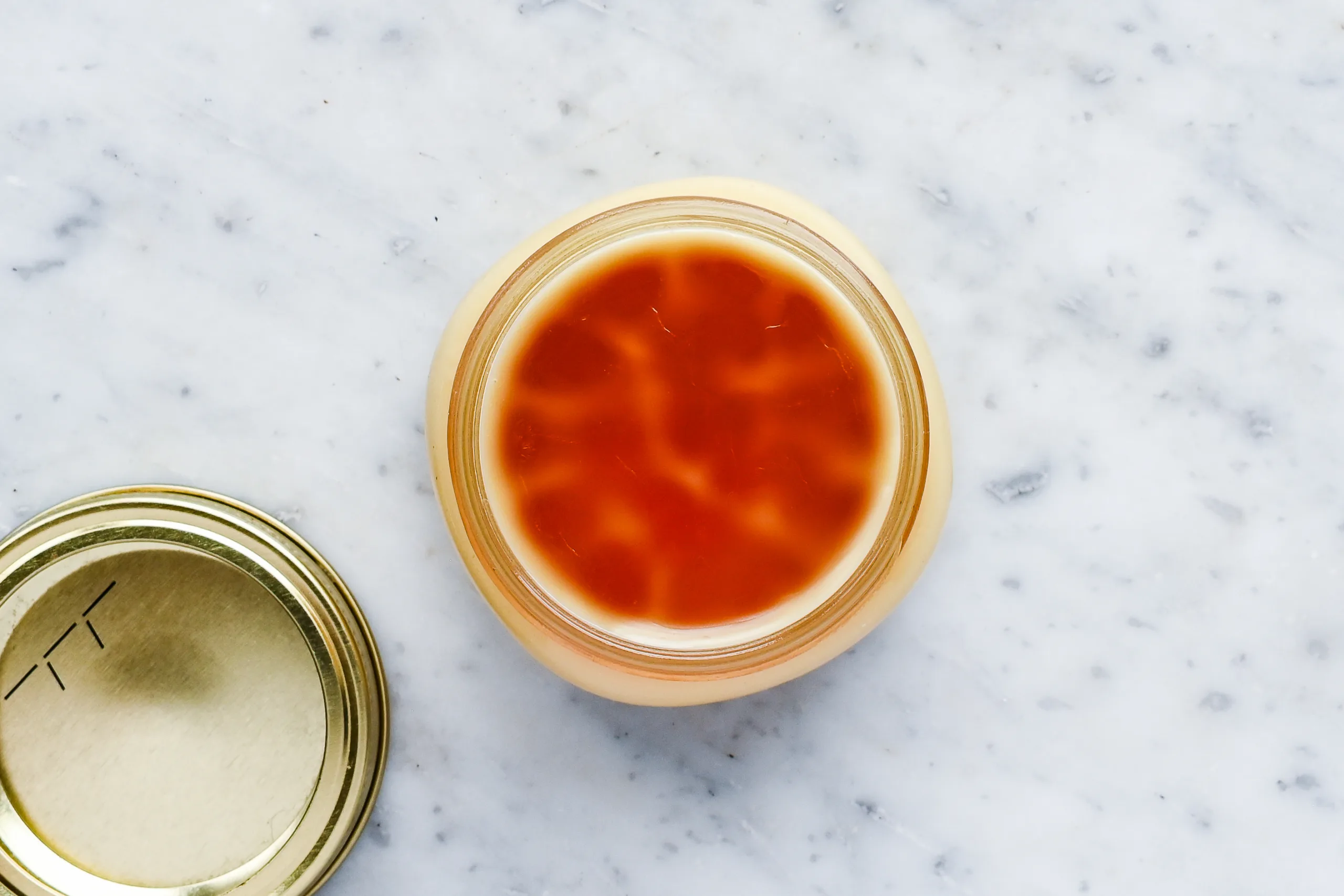 Top view of homemade natural pomade made with beeswax and tallow set in a small glass jar on a marble countertop.