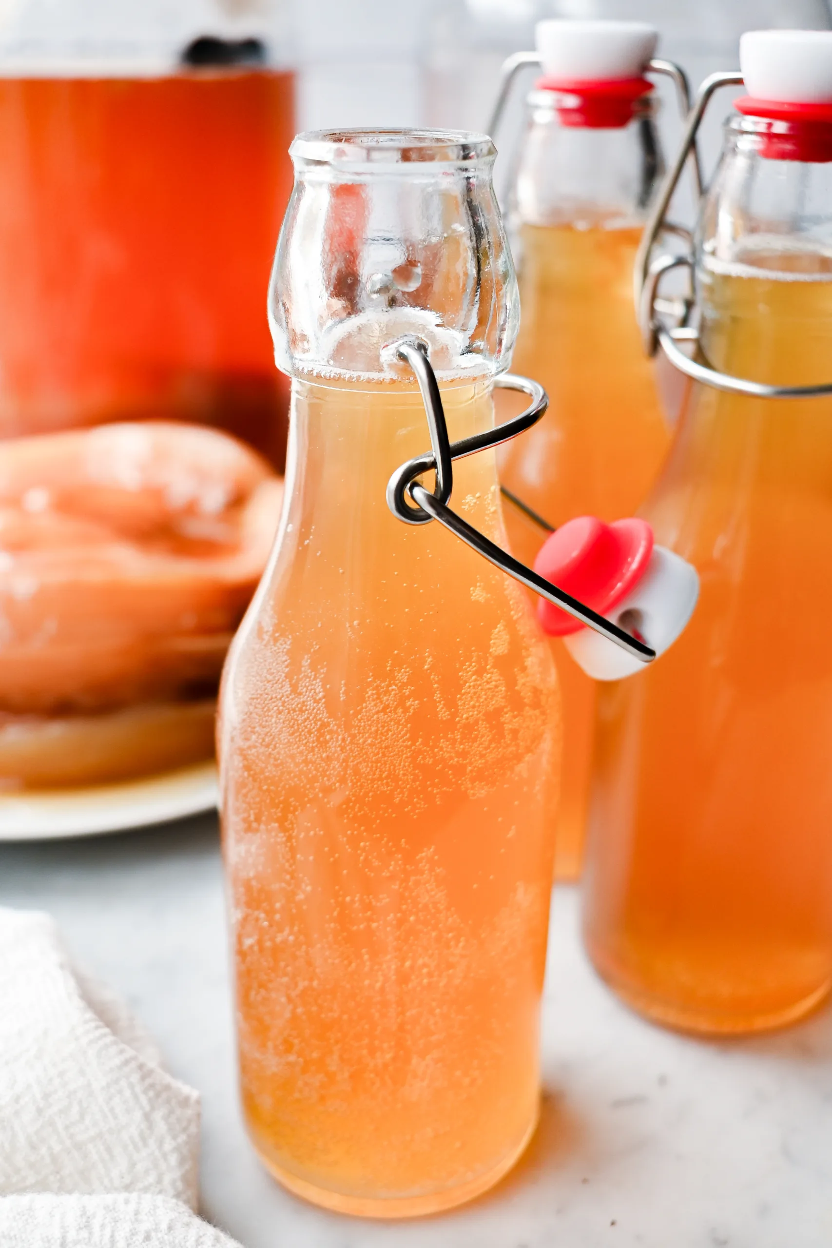 Sparkling homemade kombucha in glass bottles with a kombucha scoby and fermentation jar in the background.