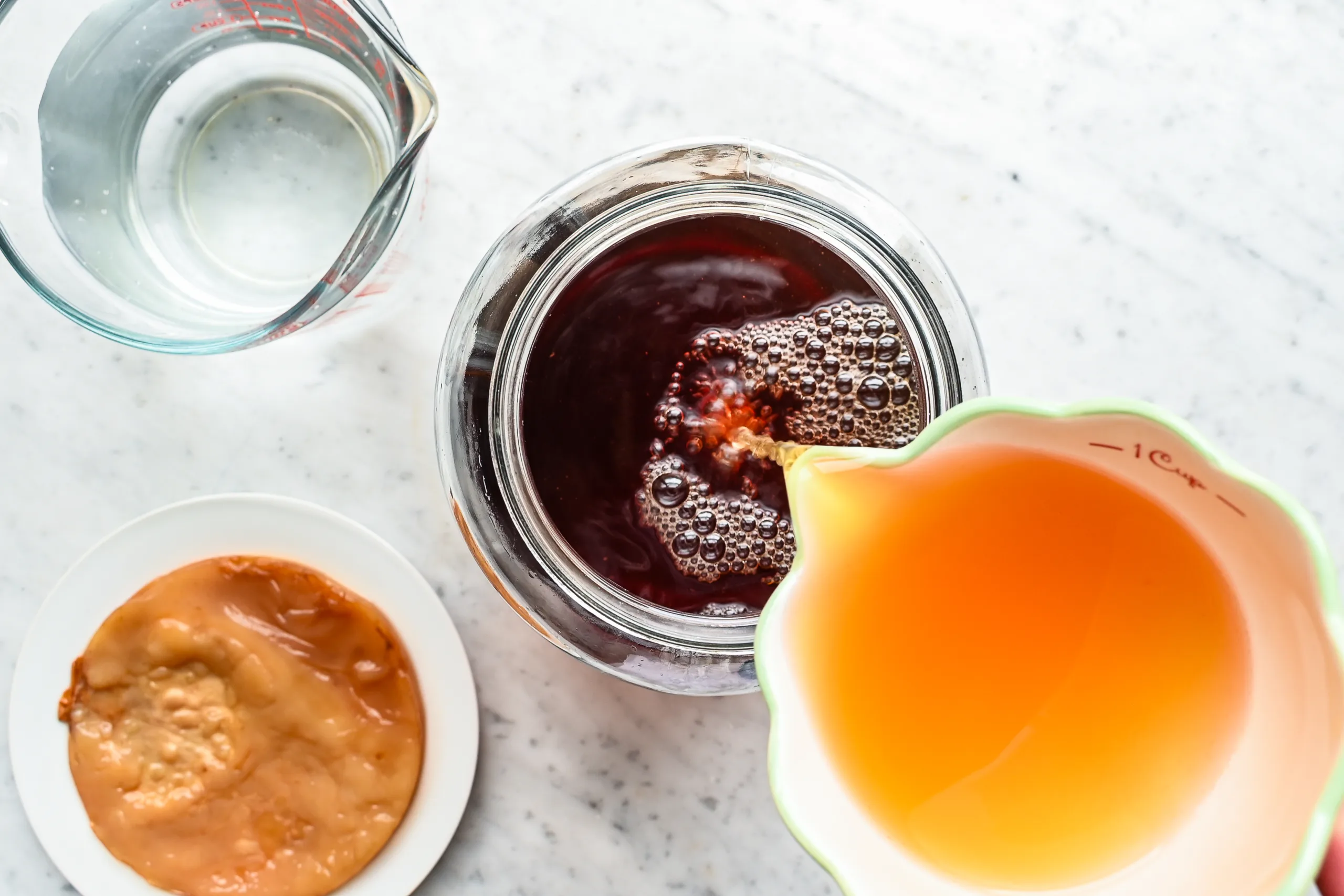 Starter tea being poured into a glass jar of sweet tea to begin homemade kombucha fermentation.