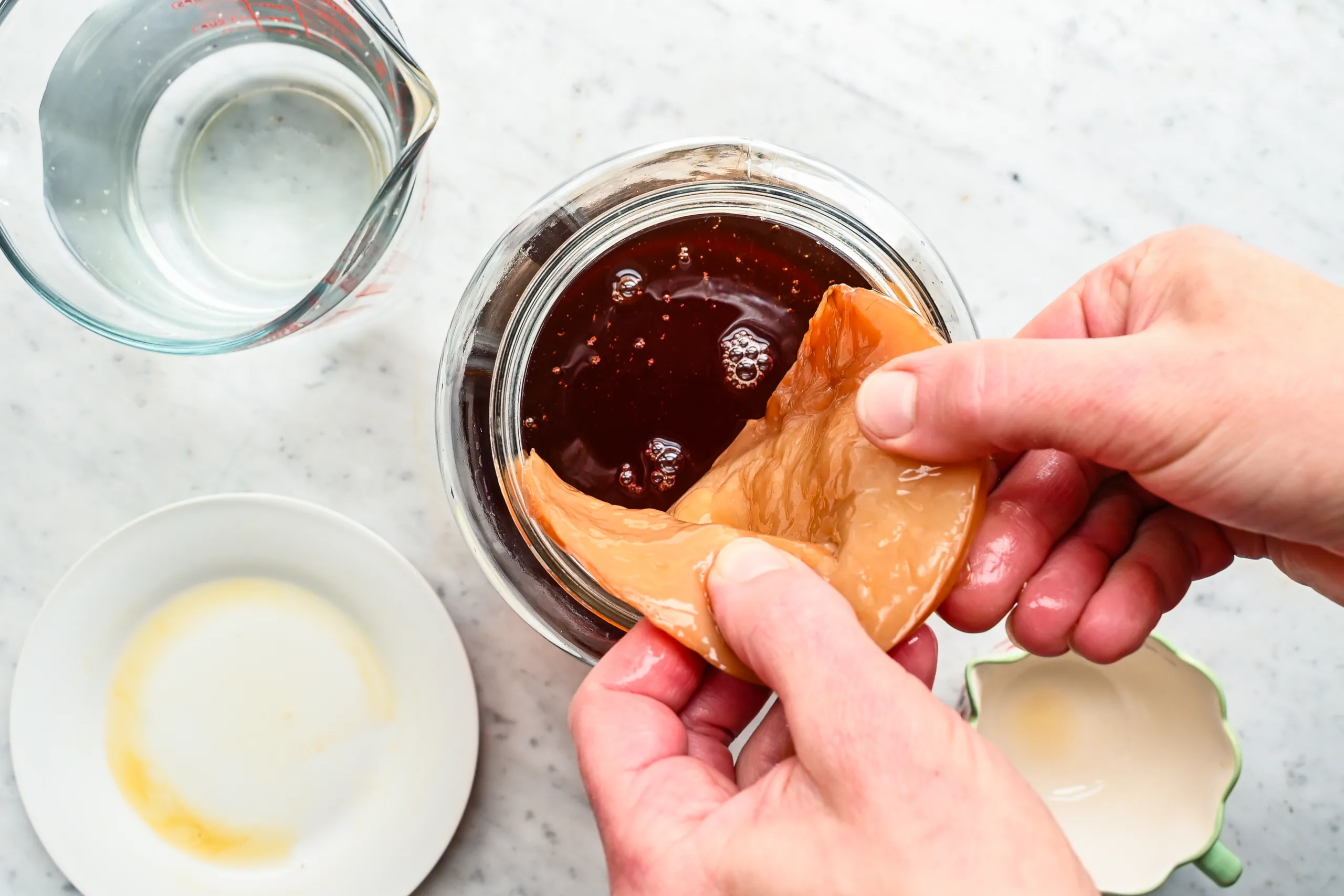 Hands placing a kombucha scoby into a jar of sweetened tea for the first fermentation.