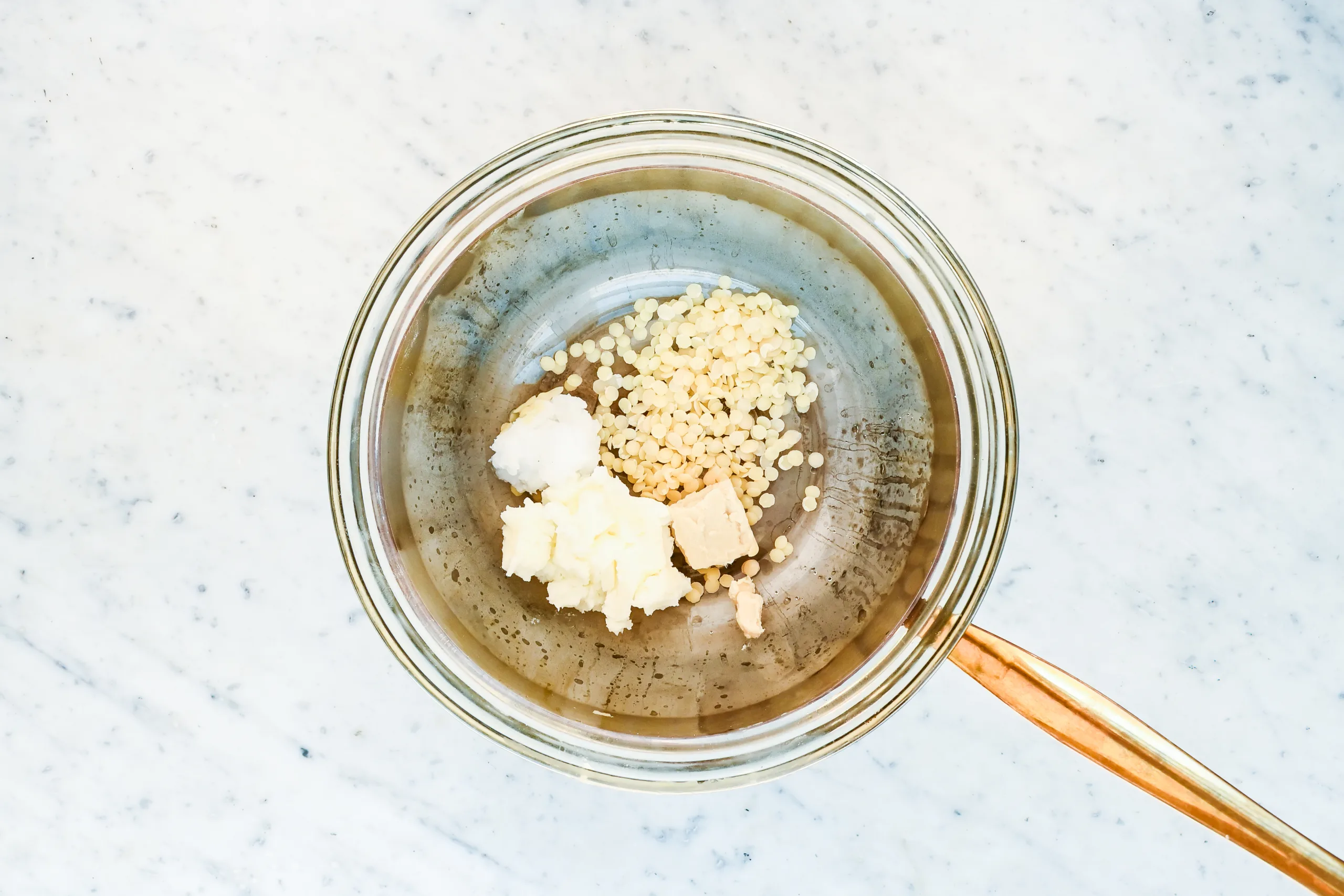 Beeswax pellets and tallow melting in a double boiler for a homemade natural deodorant recipe.