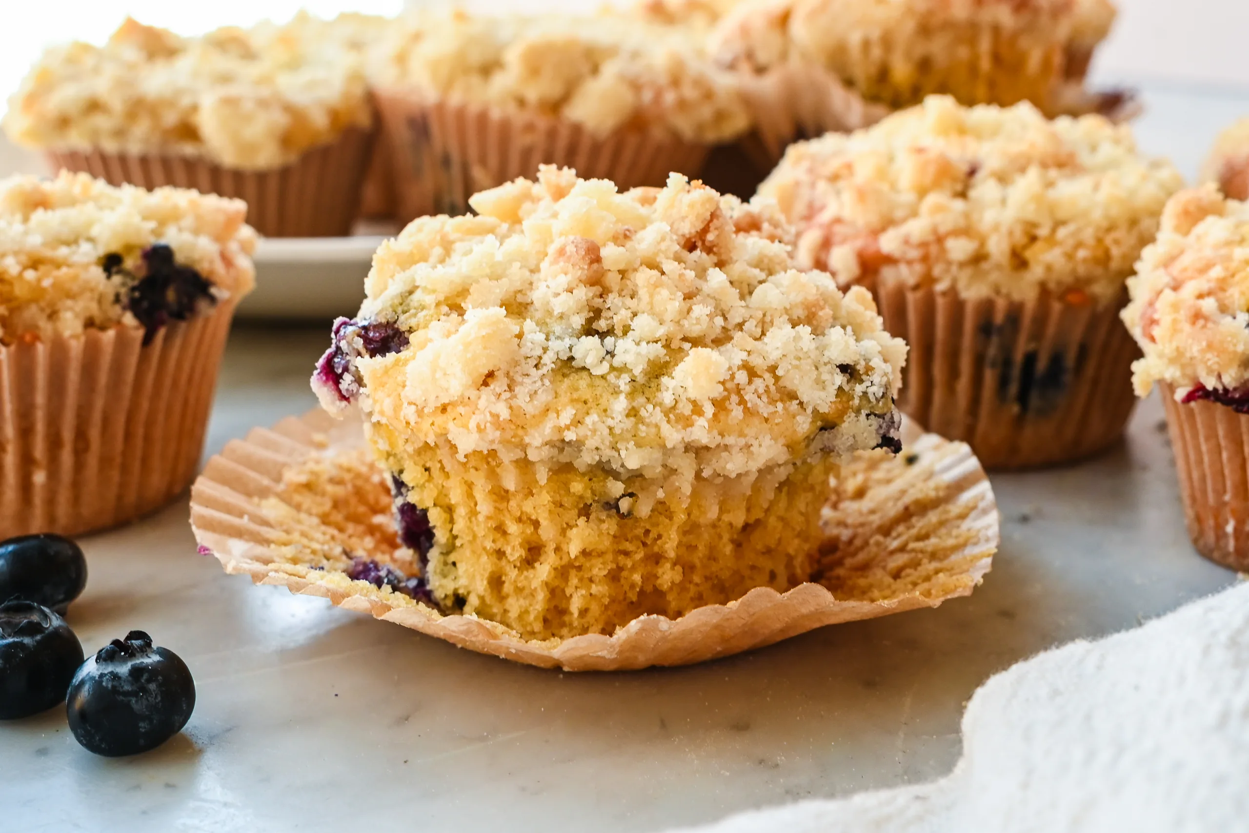 Sourdough discard blueberry muffin with crumb topping partially unwrapped to show the soft interior filled with blueberries.