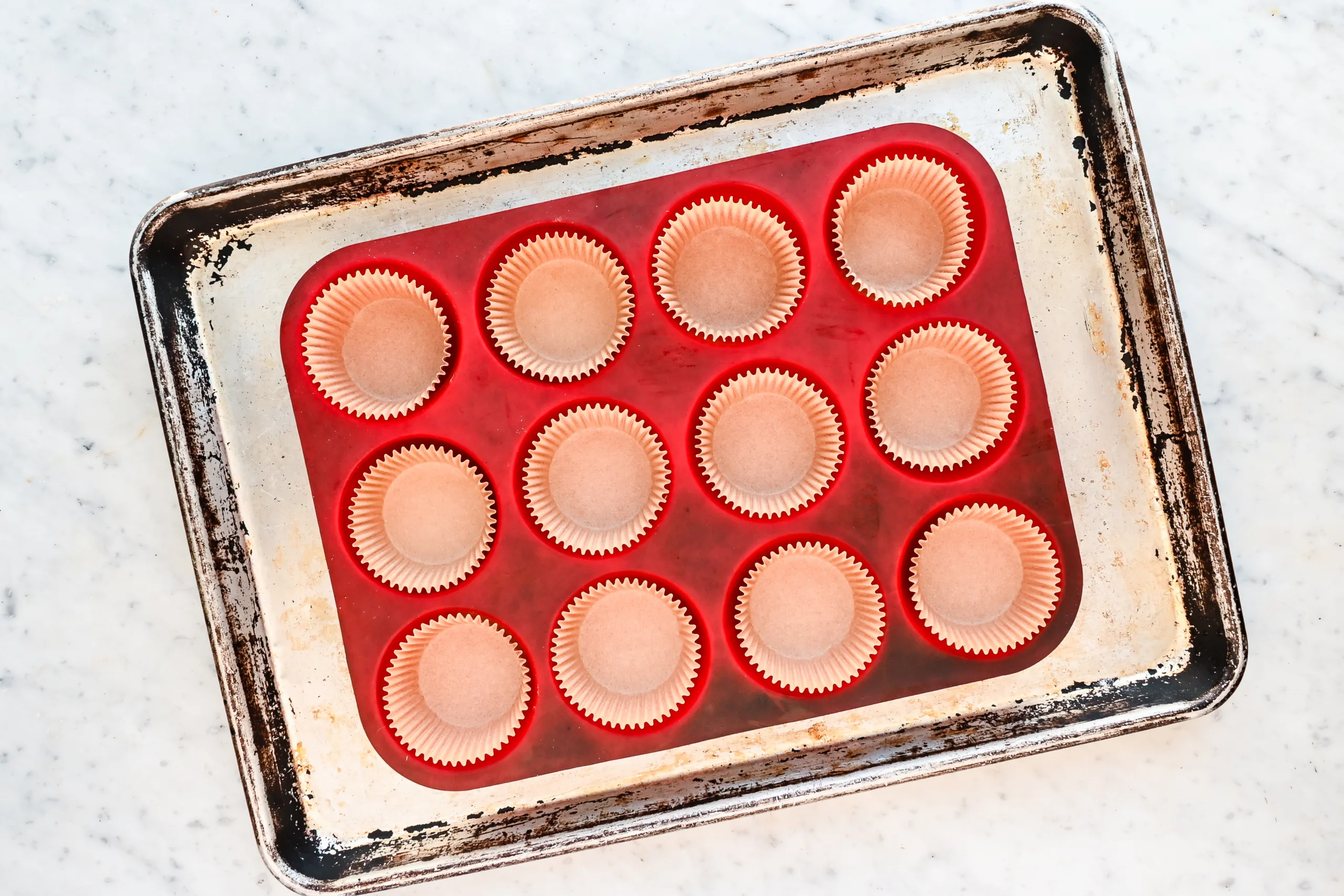 Paper muffin liners arranged in a red silicone muffin pan set on a well-used baking sheet, ready for sourdough discard blueberry muffin batter.