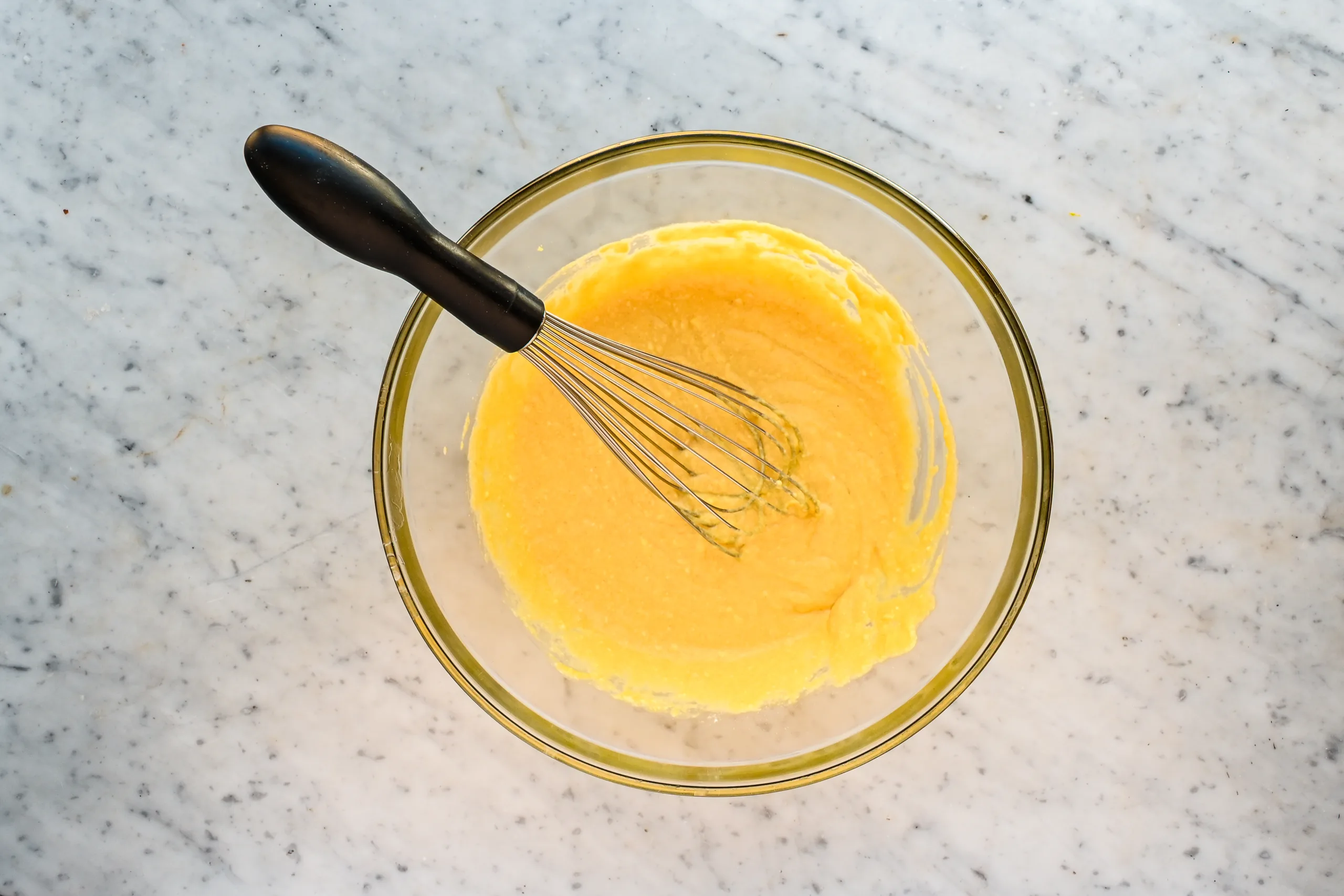Smooth muffin batter for sourdough discard blueberry muffins in a glass mixing bowl on a marble countertop with a whisk.