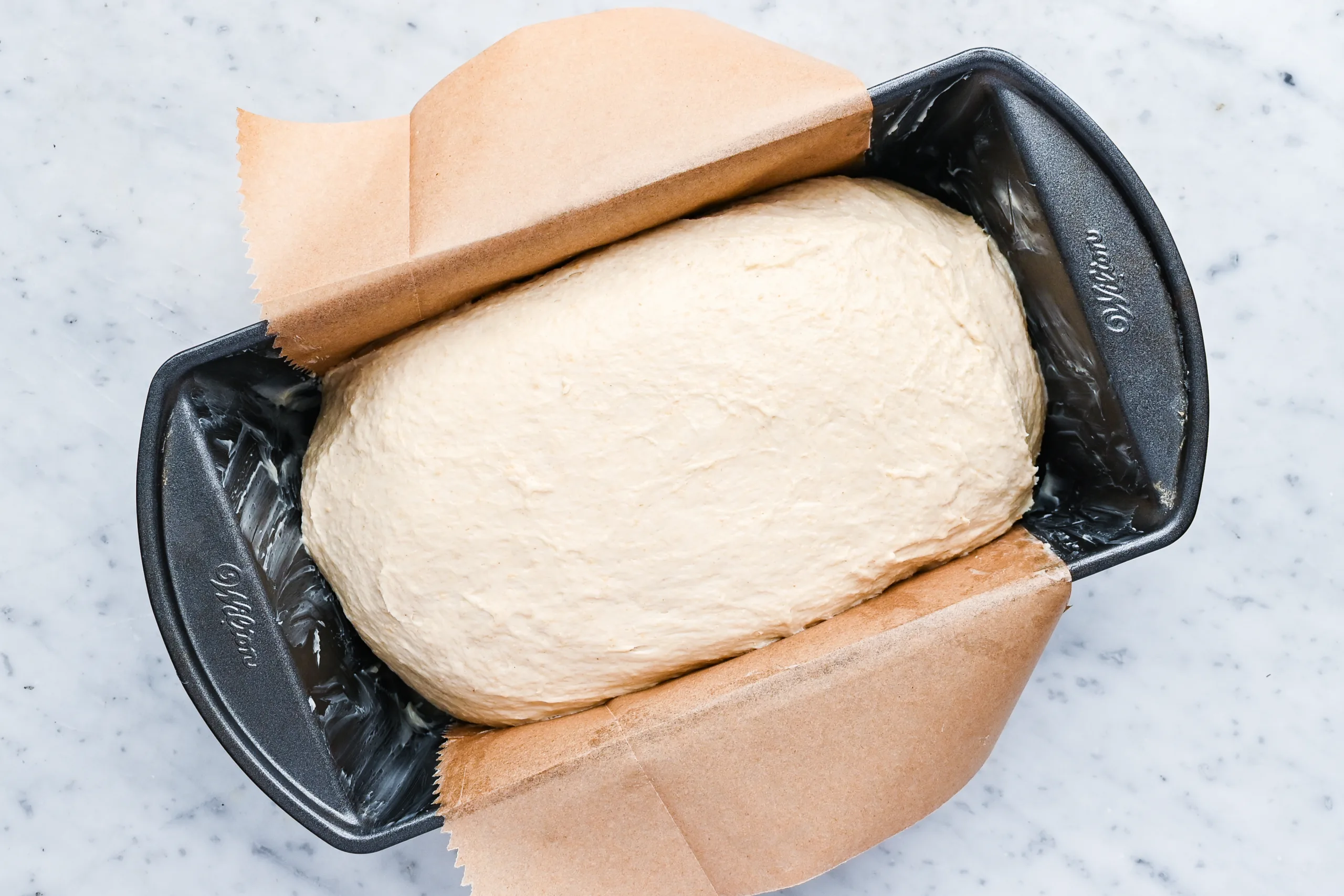 Shaped sourdough discard sandwich bread dough placed into a loaf pan lined with parchment paper.