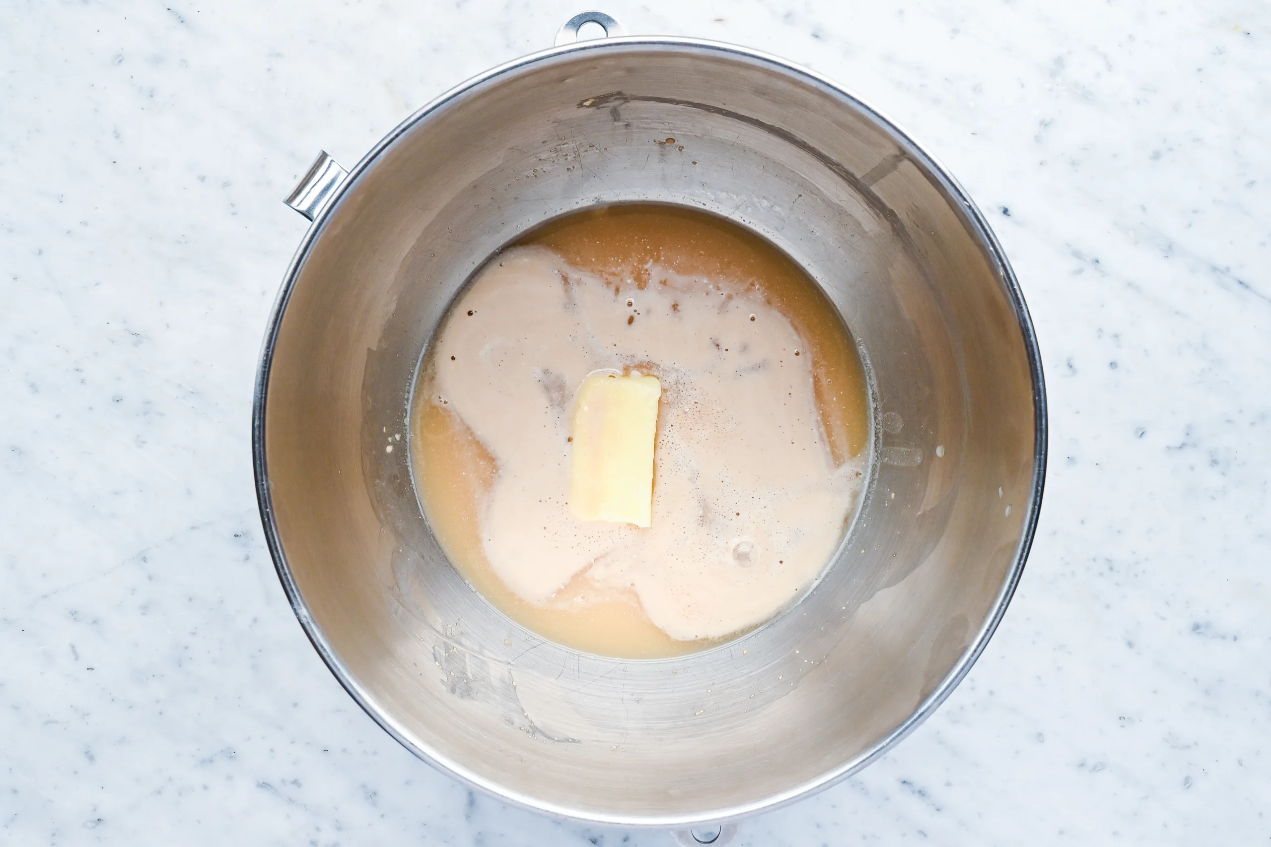 Wet ingredients for sourdough discard sandwich bread including water, butter, and sugar in a mixing bowl.
