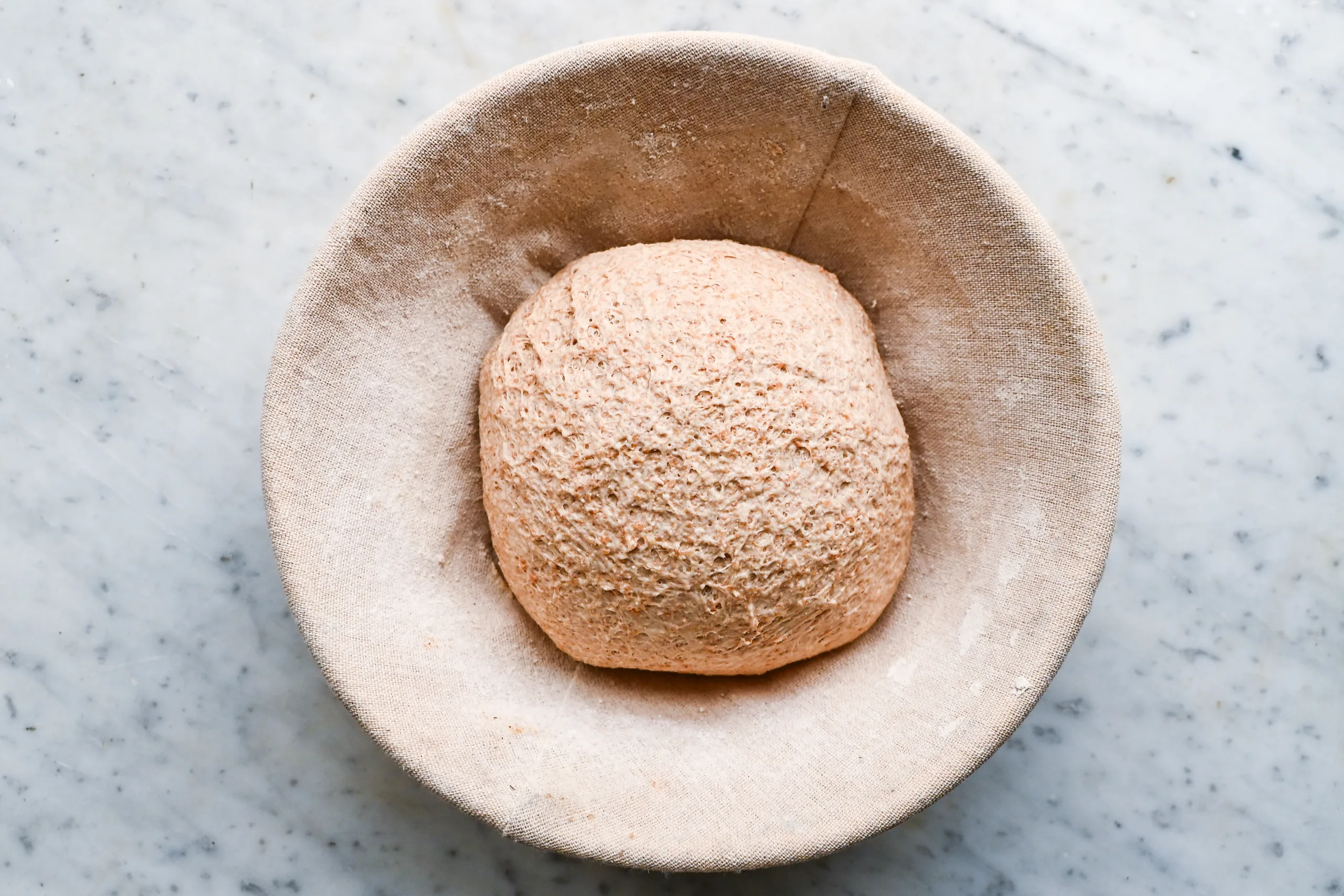 Shaped spelt sourdough loaf resting in a cloth-lined proofing banneton before baking.
