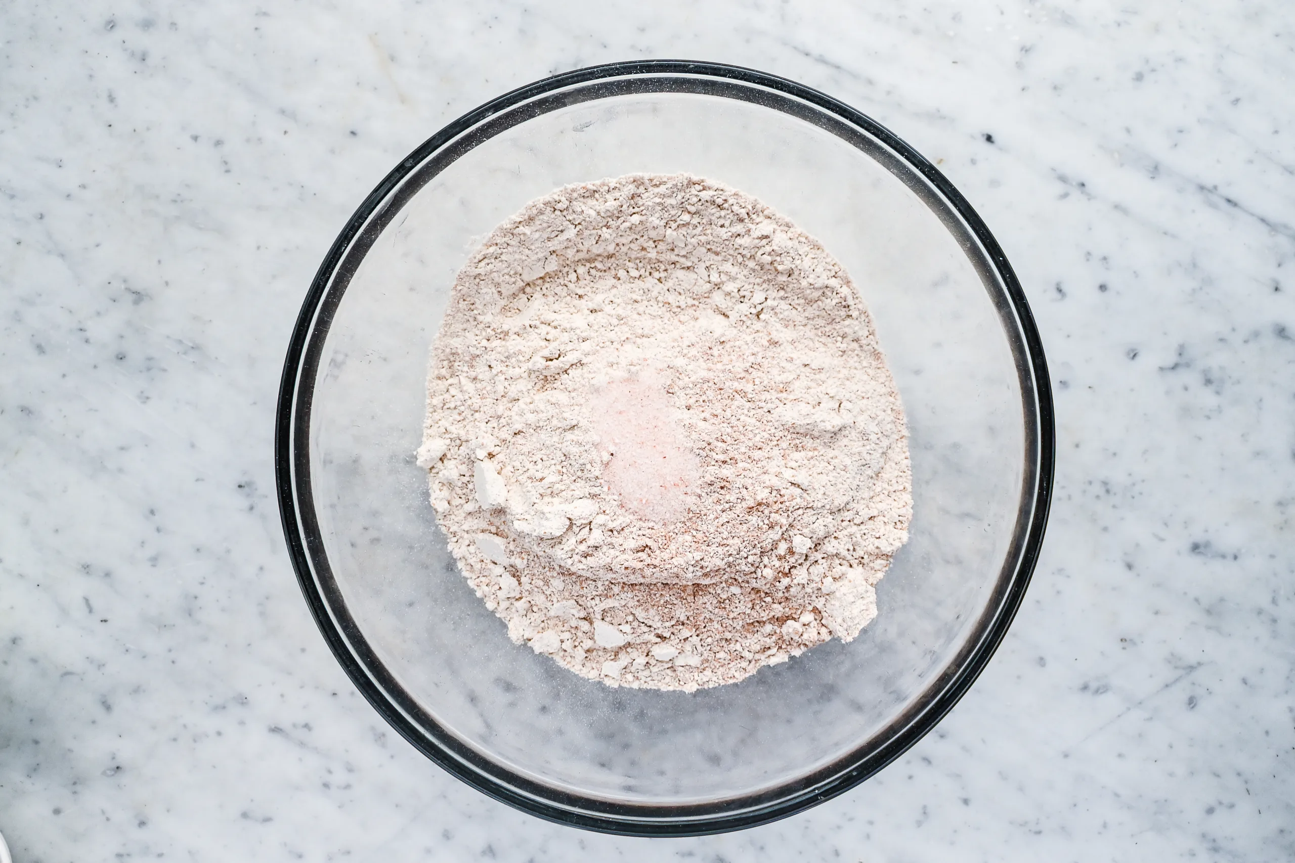 Fresh milled spelt flour and salt combined in a glass mixing bowl for sourdough bread.