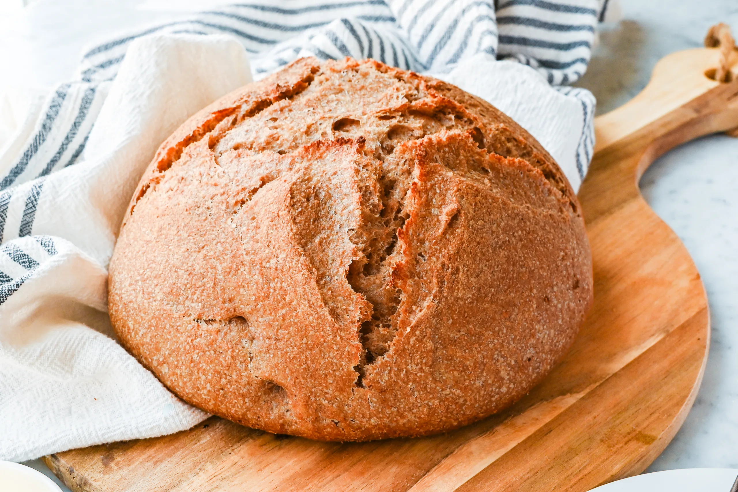 Side view of a round spelt sourdough loaf with a golden crust on a wooden cutting board.