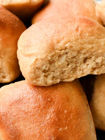 Soft whole wheat dinner rolls stacked close together, with one roll torn open to show the fluffy interior and tender crumb.