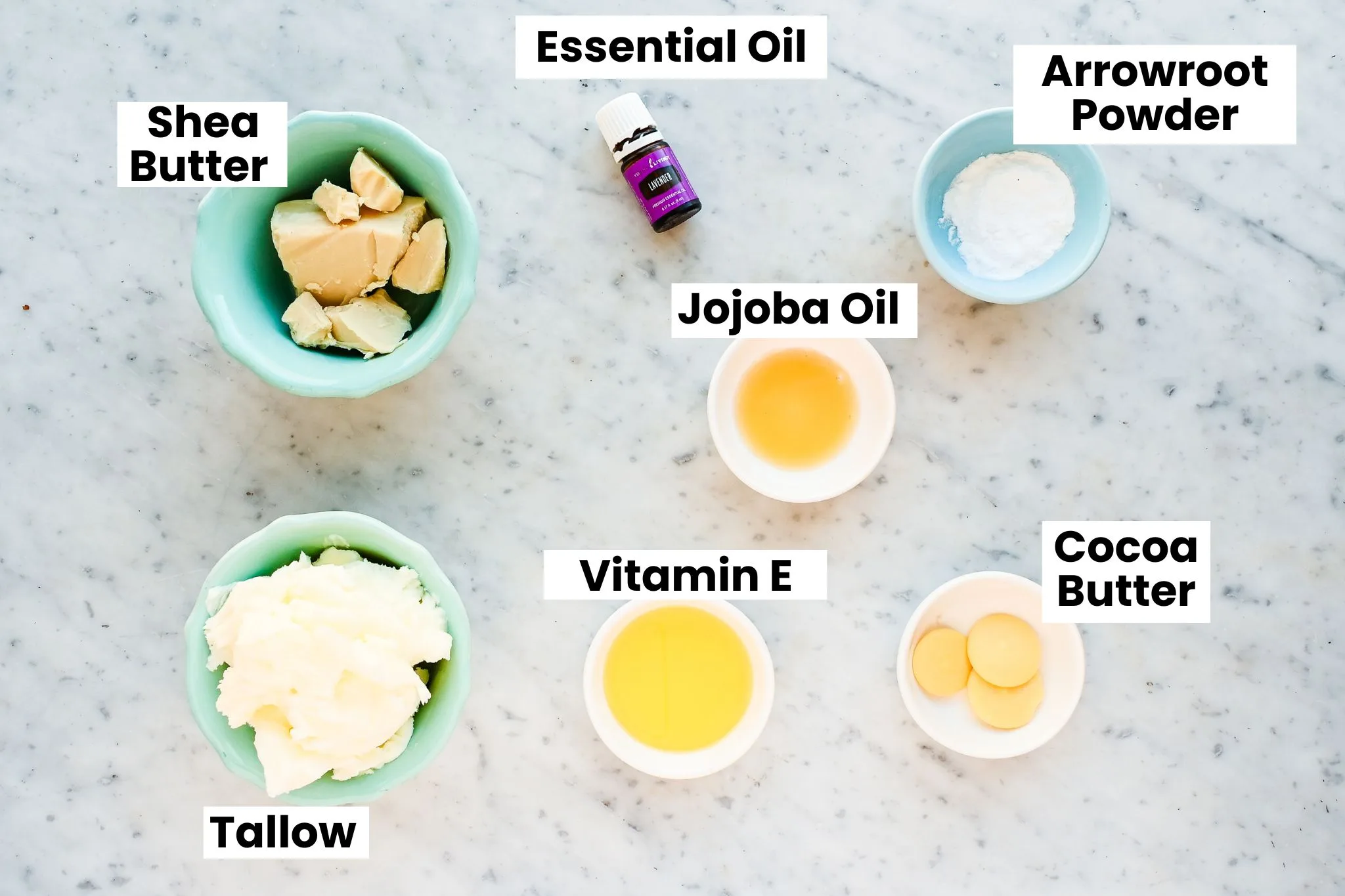 Ingredients for whipped tallow body butter arranged on a marble countertop, including tallow, shea butter, cocoa butter, vitamin E oil, arrowroot powder, and lavender essential oil.