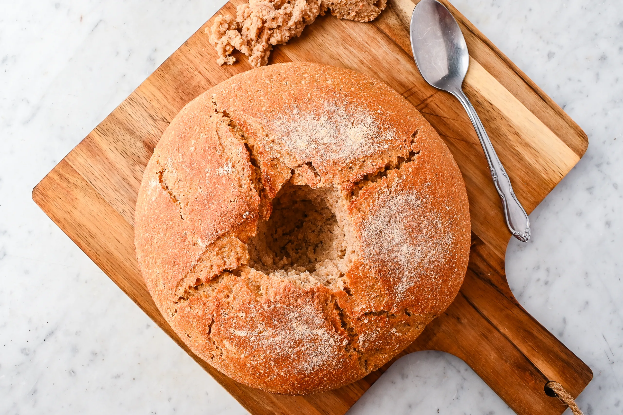 Round boule hollowed out in the center with a spoon, ready for a butter candle, on a wooden board with the removed bread pieces nearby