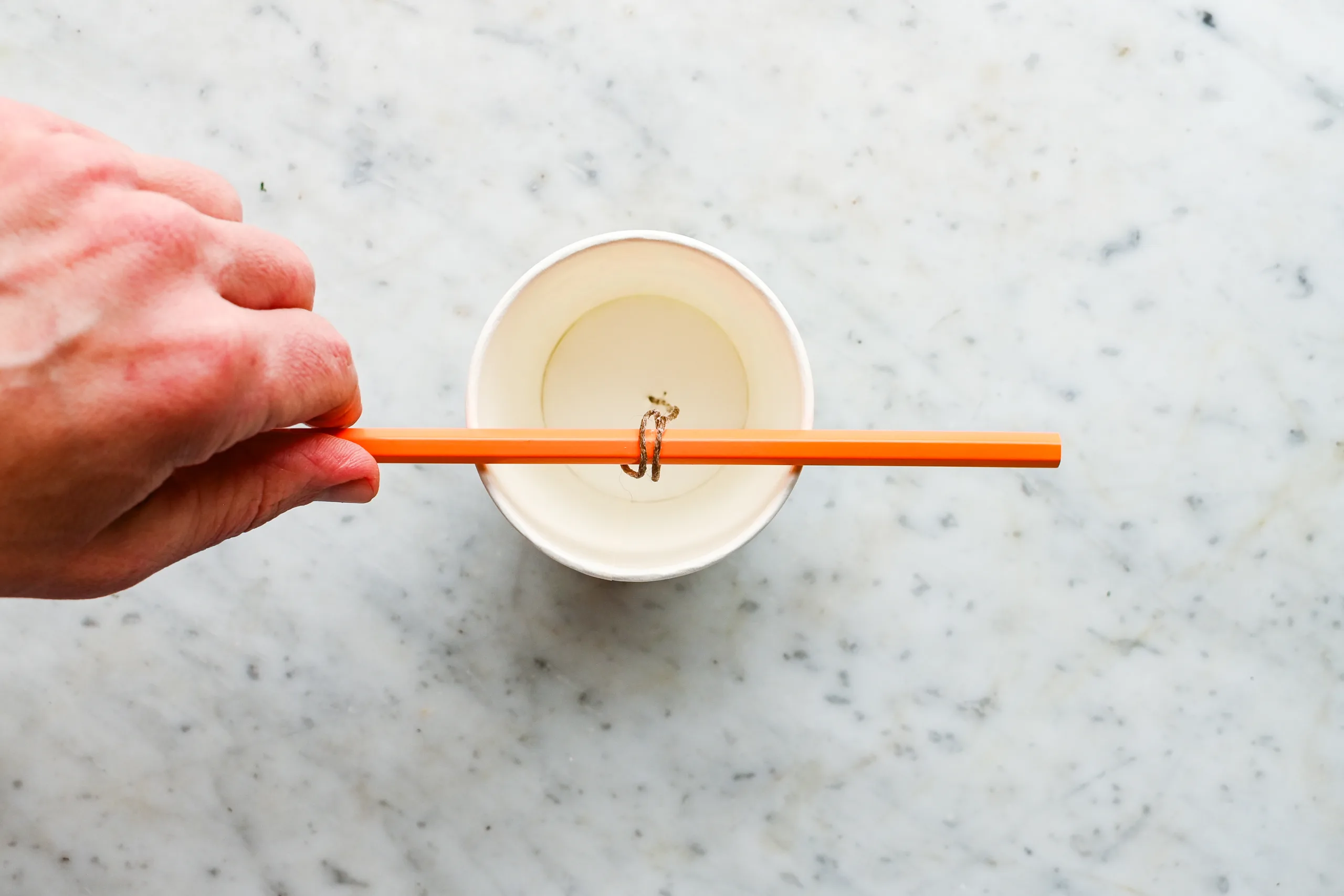 Food-safe wick threaded through the bottom of a paper cup and held upright with a pencil across the top