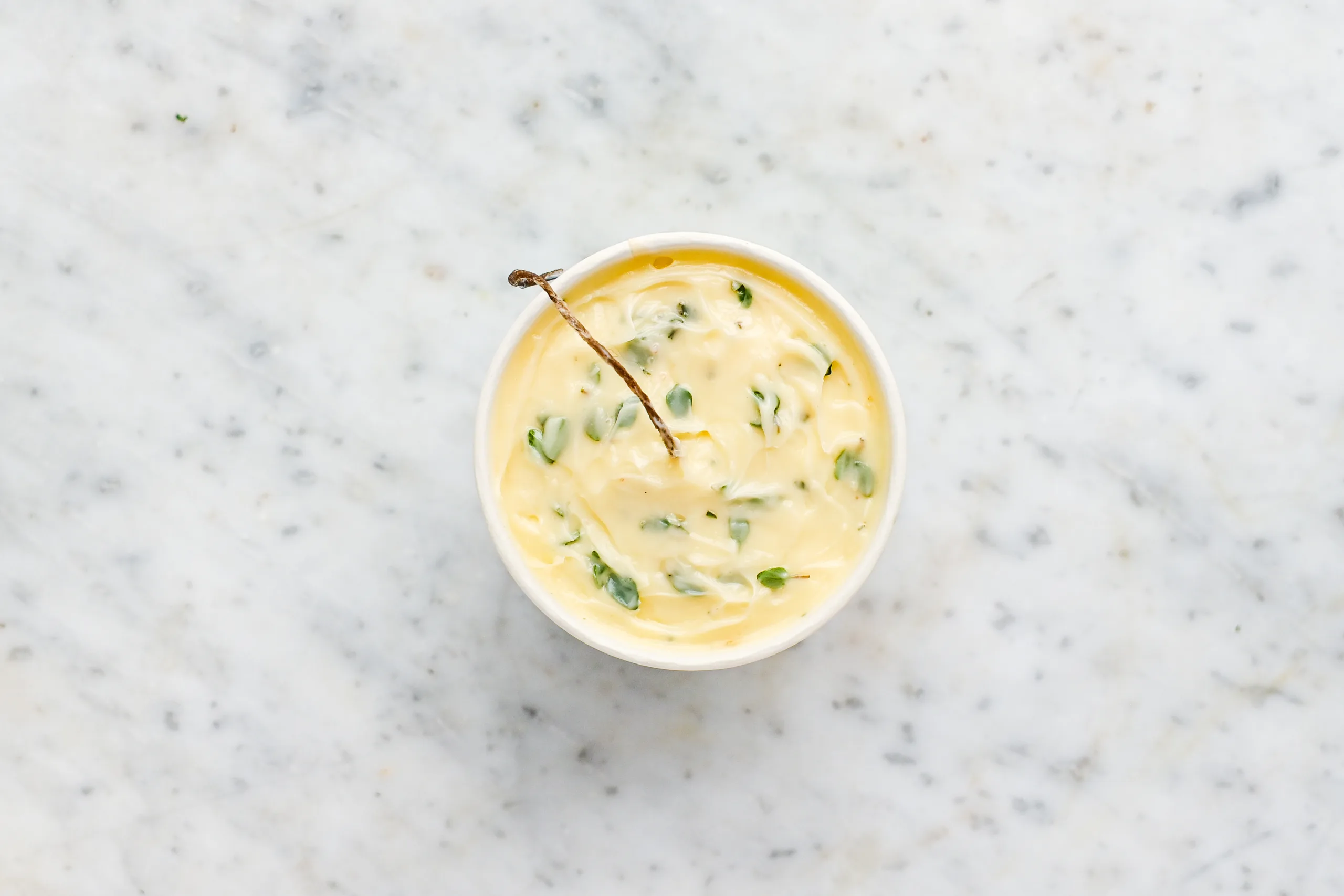 Finished unlit garlic herb butter candle in a paper cup with a centered wick, viewed from above on a marble surface.