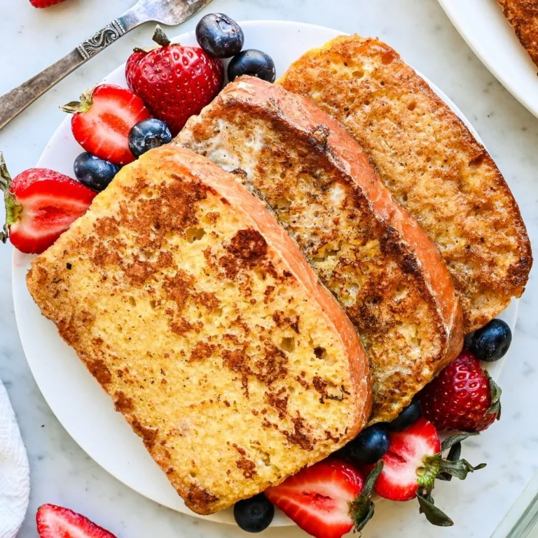Sourdough French toast served on a white plate with fresh strawberries and blueberries.