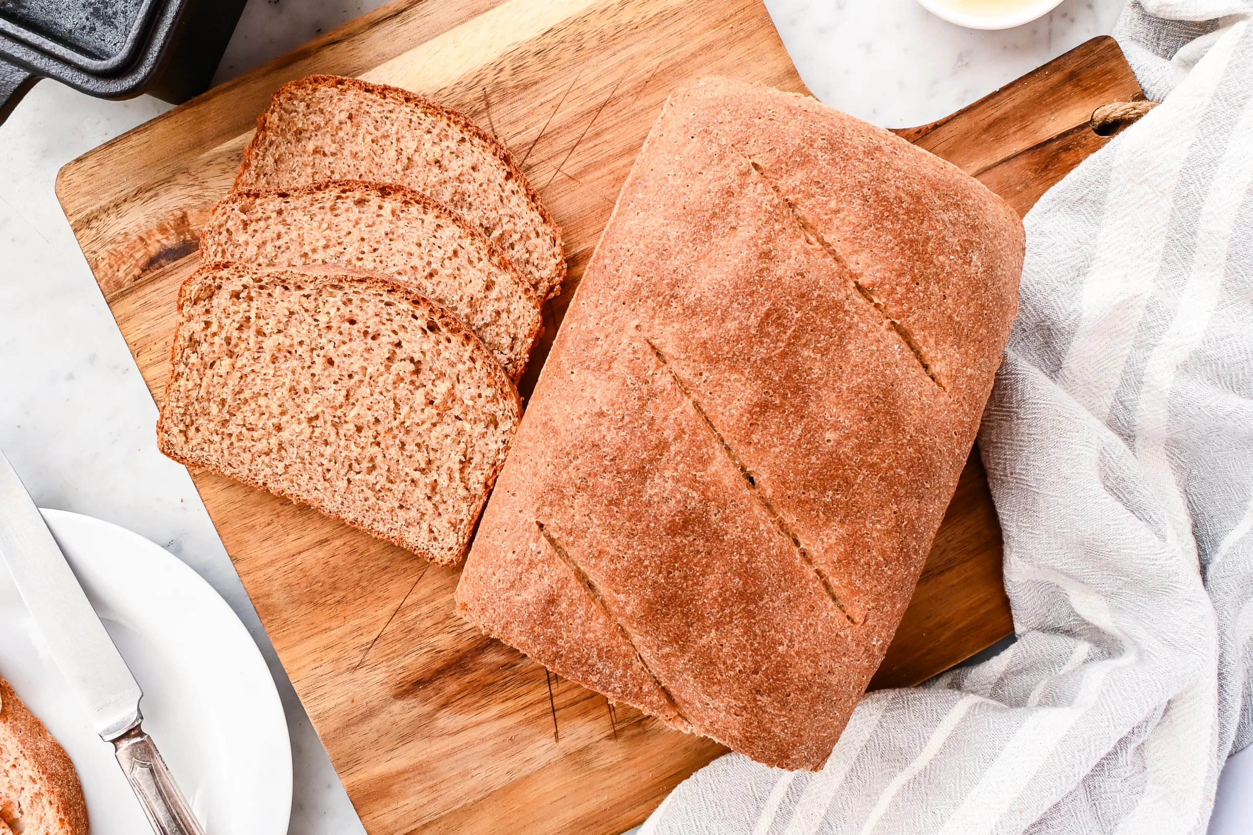 Whole grain spelt sandwich bread loaf with sliced bread and butter on a wooden serving board.