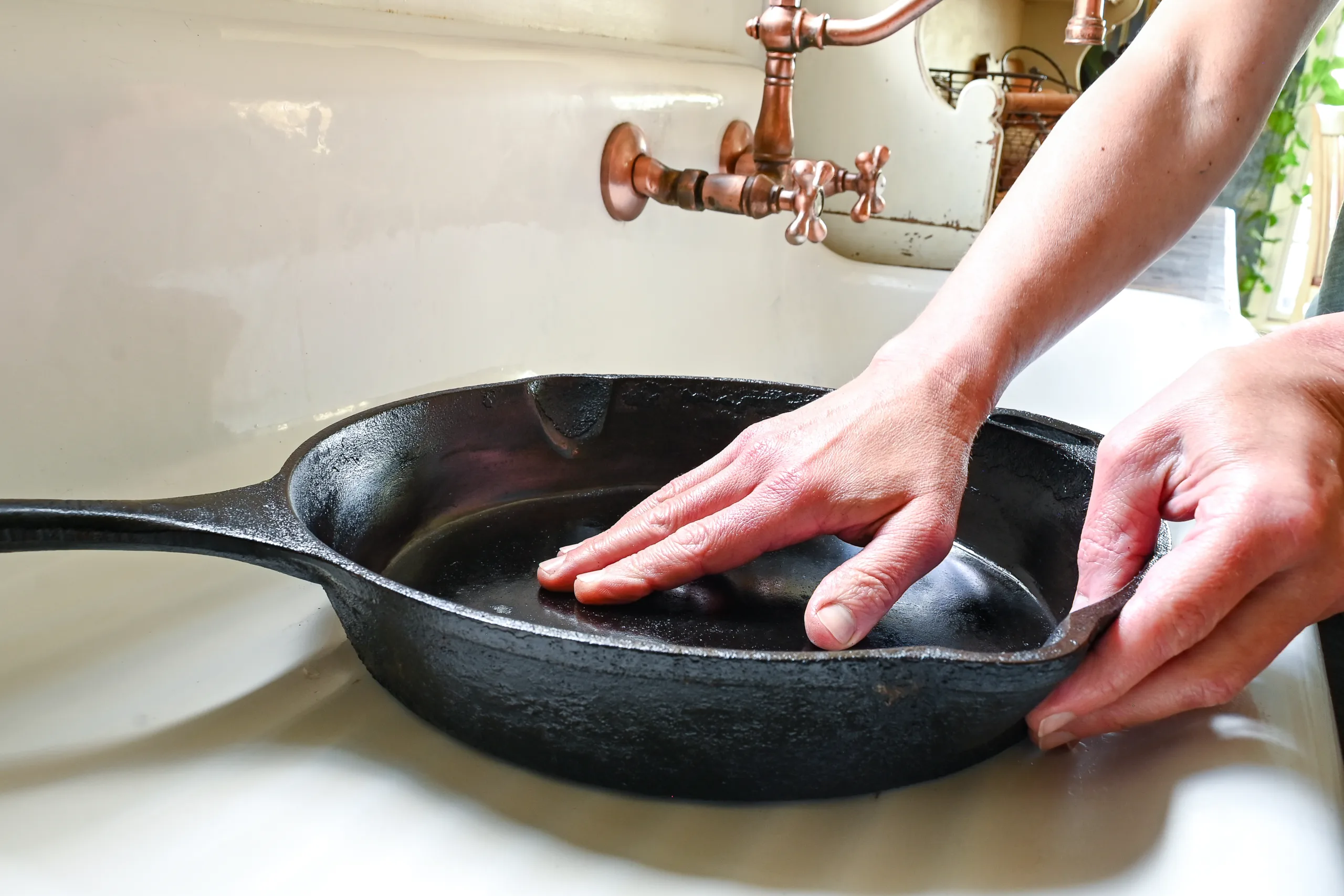 Hand rubbing oil on the inside of a clean cast iron skillet to show the smooth seasoned surface after cleaning