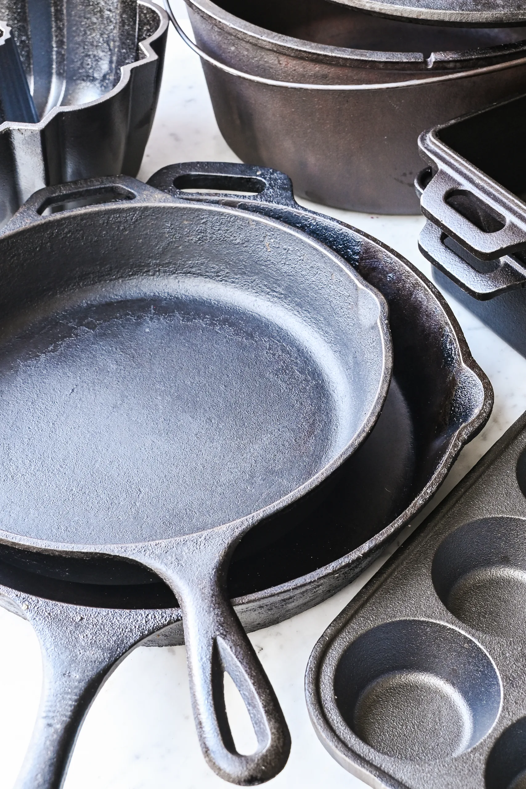 Assorted cast iron bakeware and cookware arranged together, including a skillet, loaf pans, Dutch oven, and muffin pan