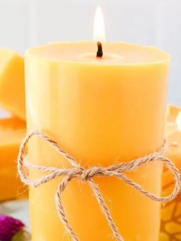 Lit handmade beeswax pillar candle tied with twine, styled with beeswax blocks and a decorative candle in the background.