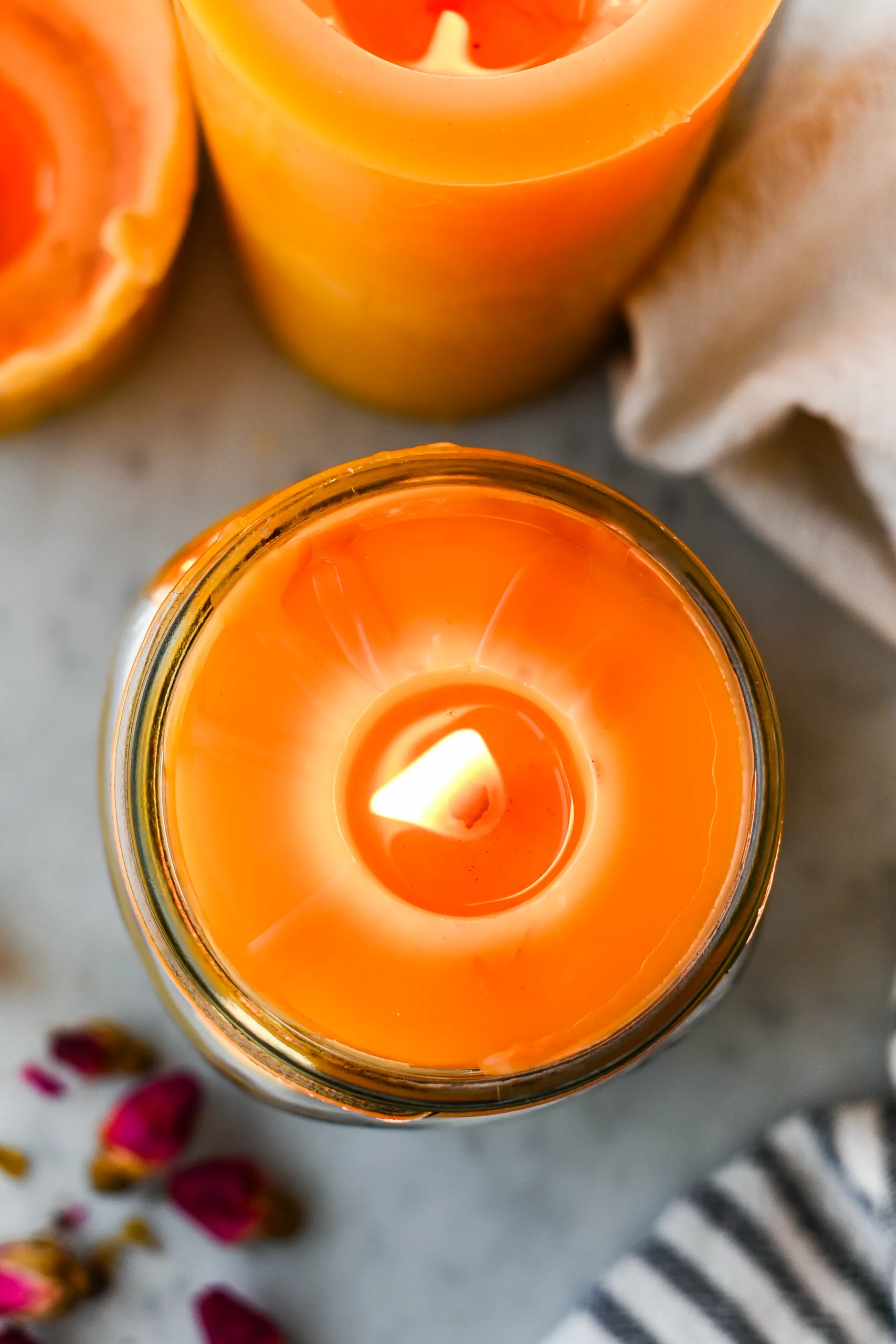 Top view of a lit beeswax candle in a mason jar, styled with rosebuds and other beeswax candles nearby