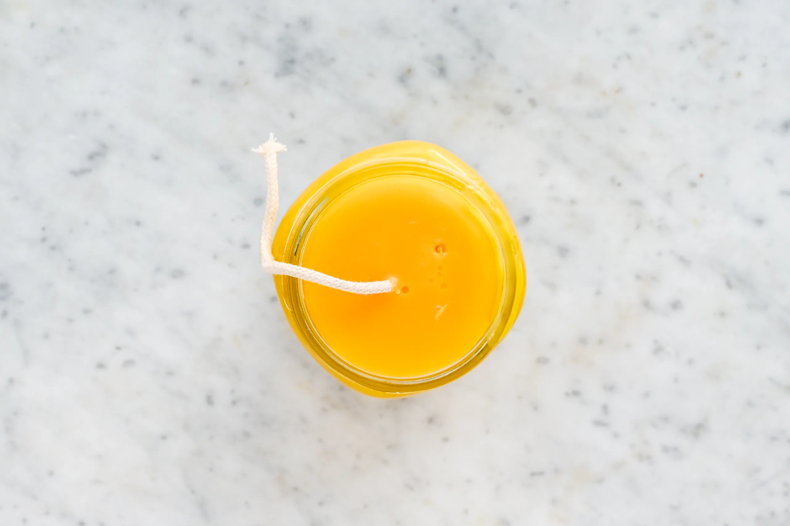 Overhead view of a mason jar filled with melted beeswax and the wick centered across the top with a pencil