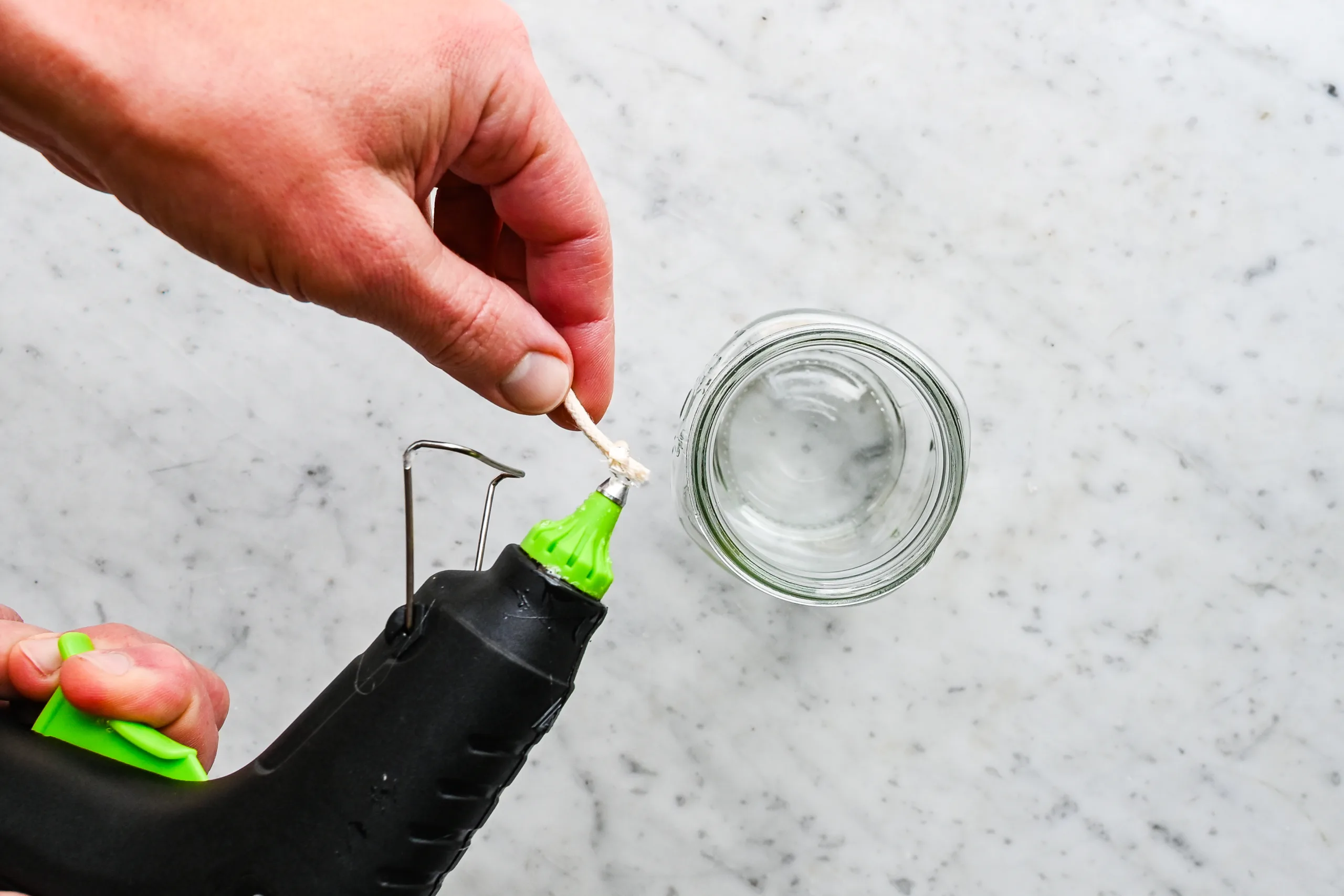 Hot glue being applied to the bottom of a candle wick before securing it inside a mason jar for a beeswax candle