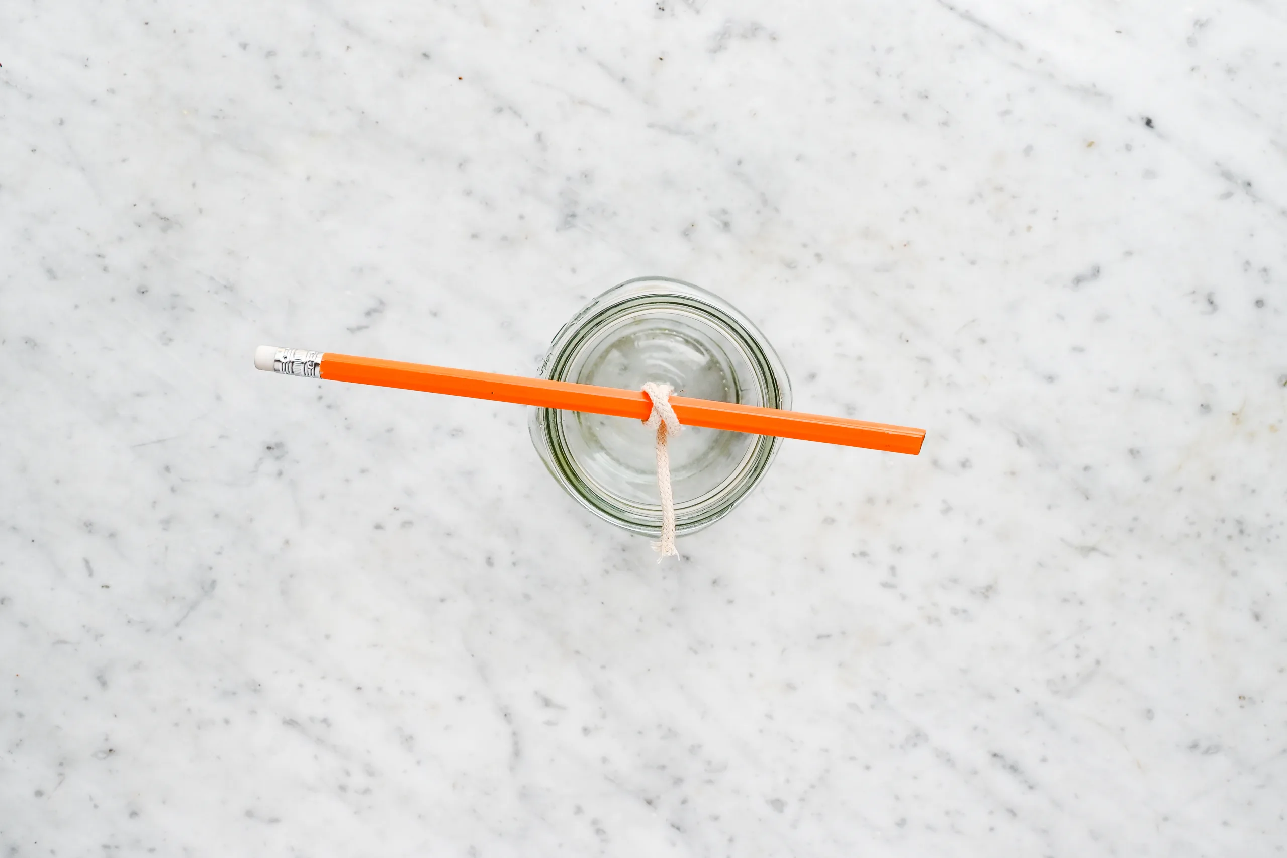 Top view of a mason jar with the candle wick centered and tied to a pencil across the opening