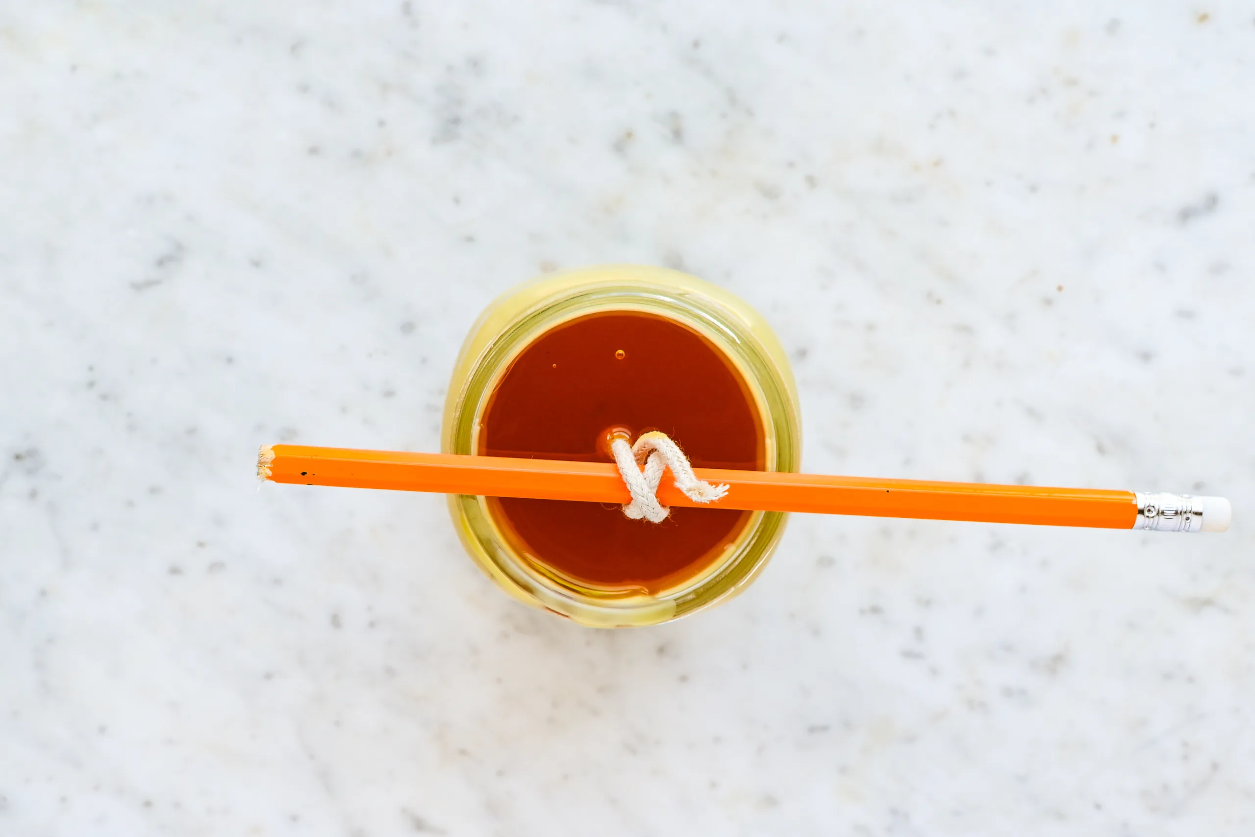 Melted beeswax poured into a mason jar with the wick centered and secured to a pencil