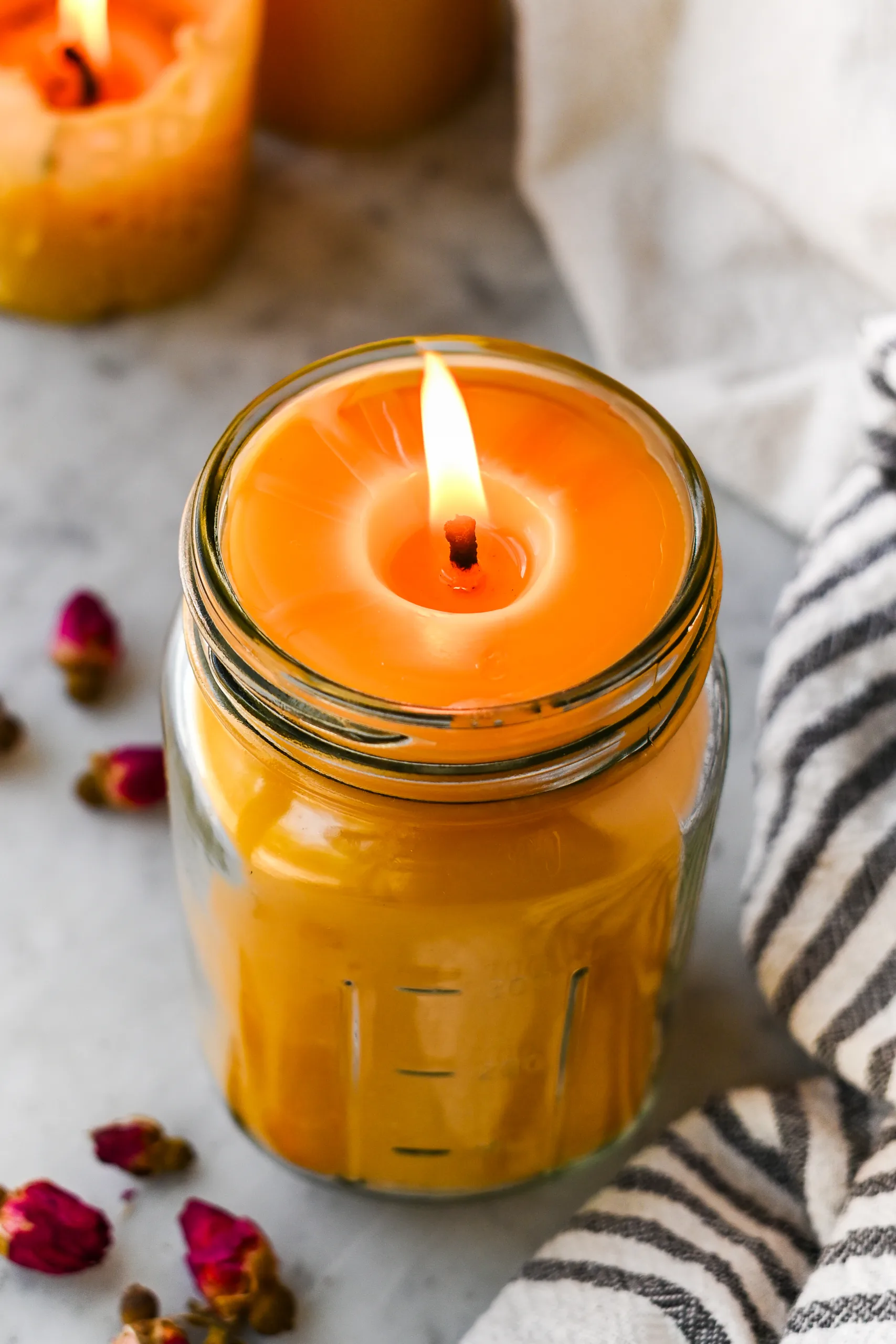 Lit beeswax candle in a mason jar with a smooth melt pool, styled with rosebuds and a striped cloth nearby