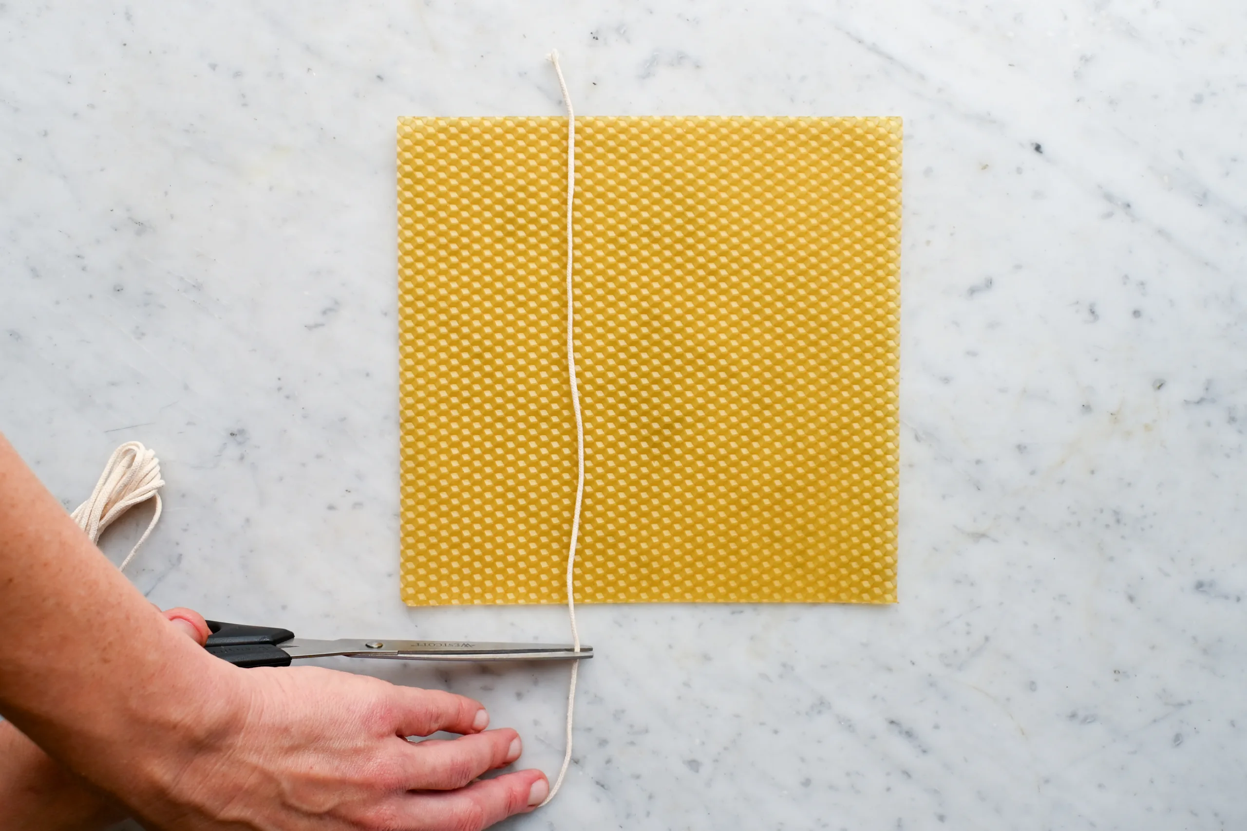 Cotton wick being measured and cut to fit a beeswax sheet for rolled beeswax candle making