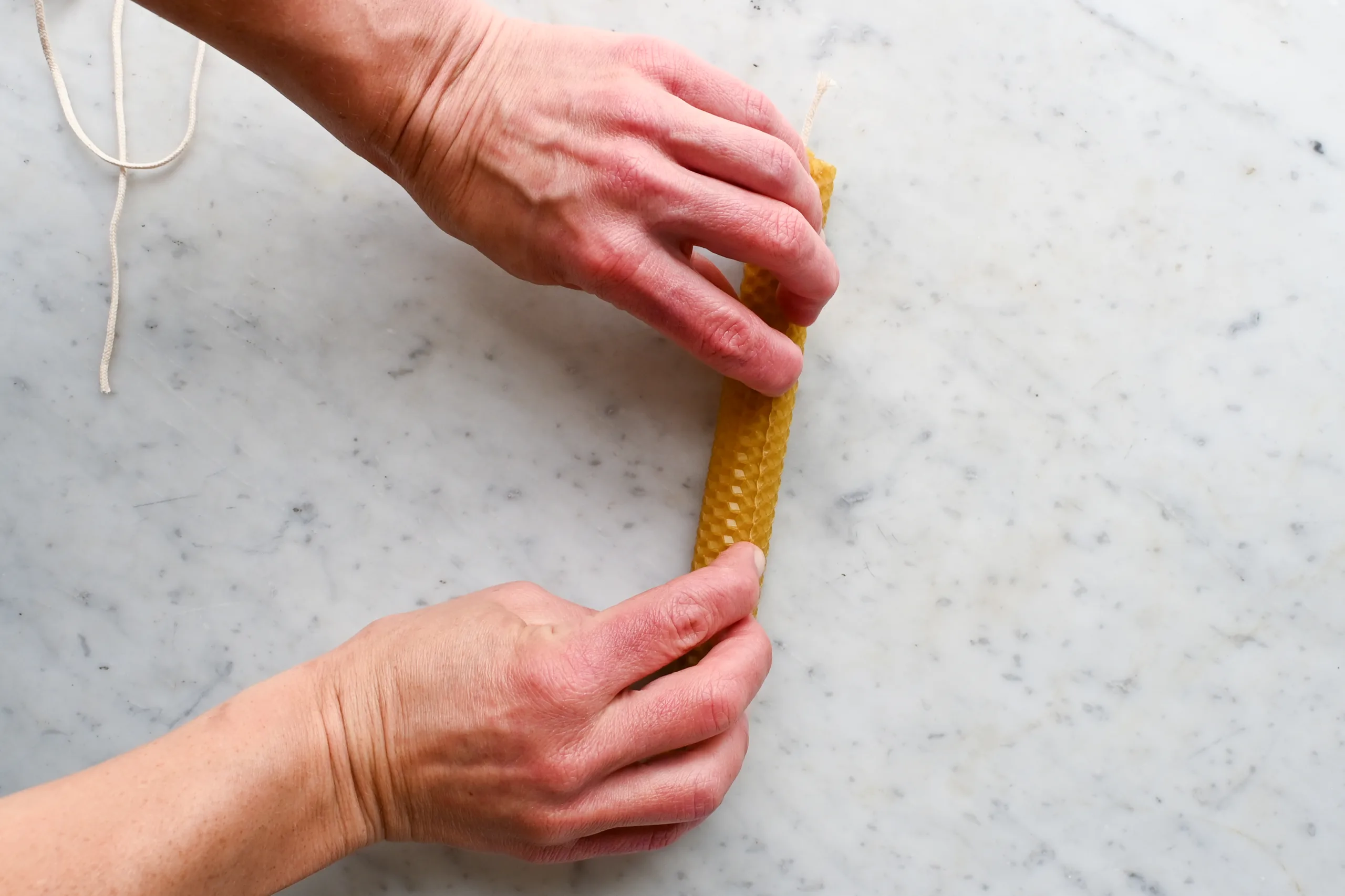 Hands rolling a beeswax sheet tightly around the wick to form an old-fashioned rolled beeswax candle