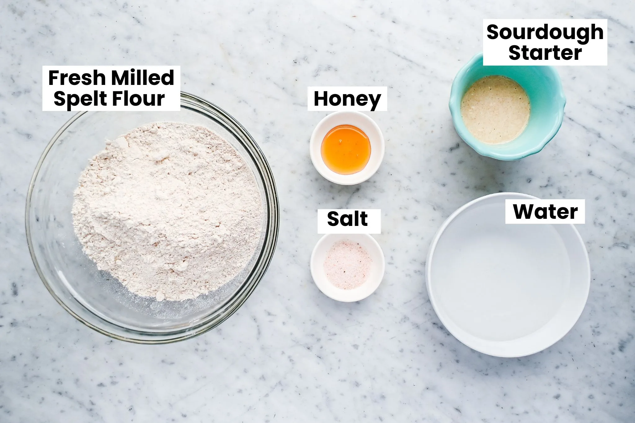 Measured ingredients for spelt sourdough bread including fresh milled spelt flour, honey, sourdough starter, salt, and water.