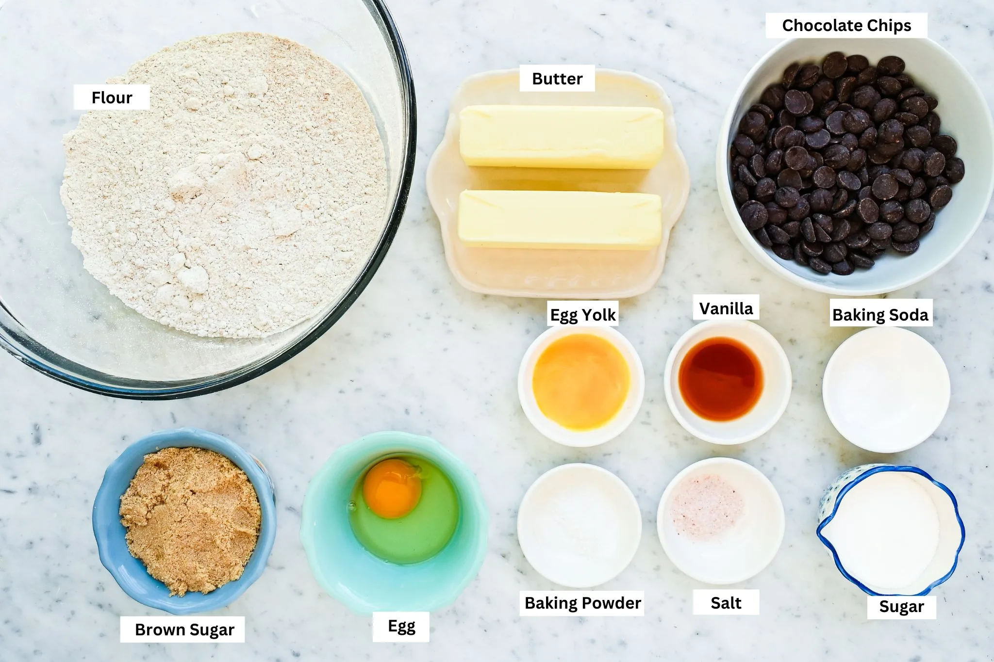 Labeled ingredients for whole wheat chocolate chip cookies with flour, butter, chocolate chips, brown sugar, egg, vanilla, baking soda, baking powder, salt, and sugar.