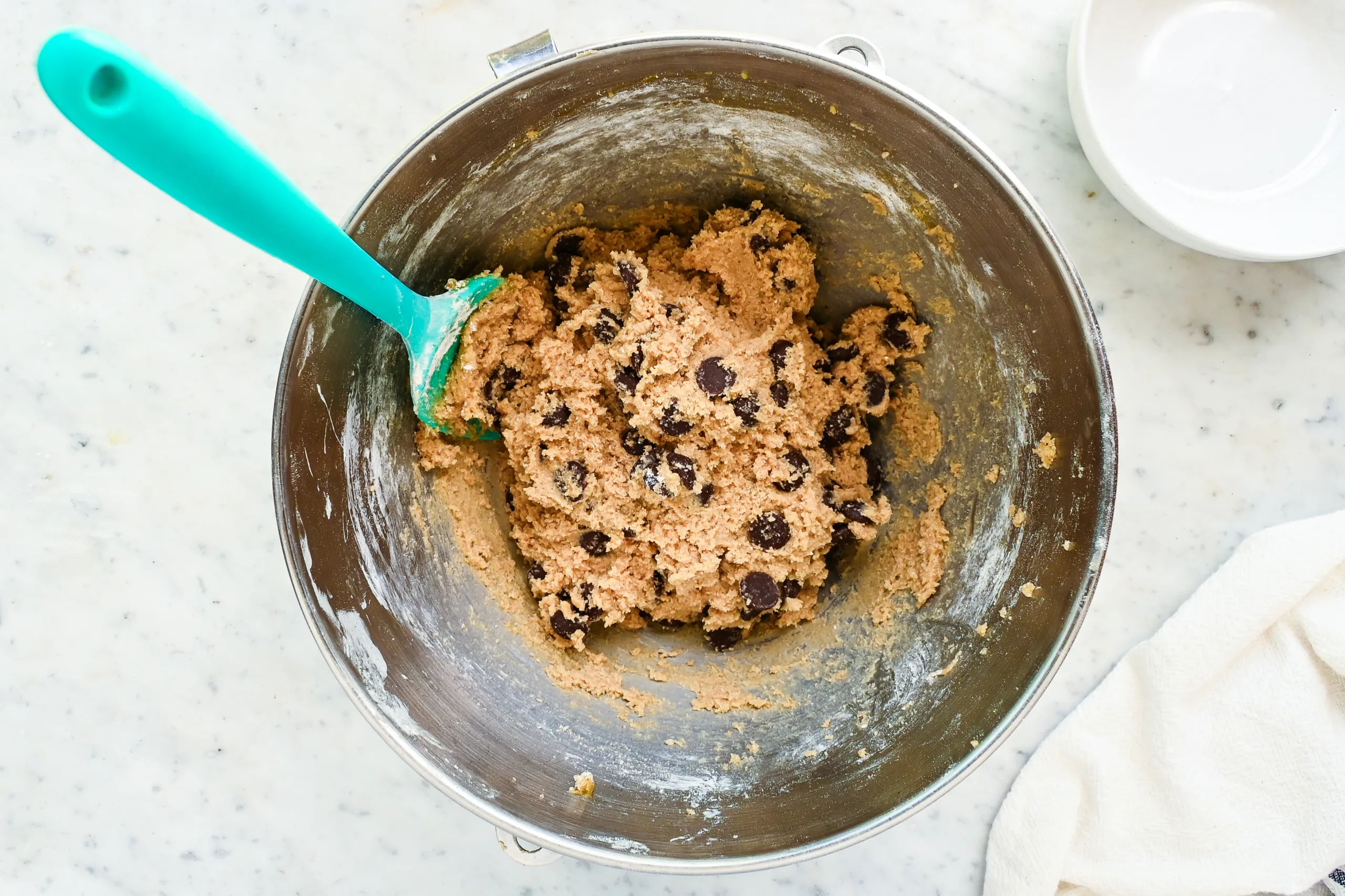 Chocolate chips folded into whole wheat cookie dough with a spatula.