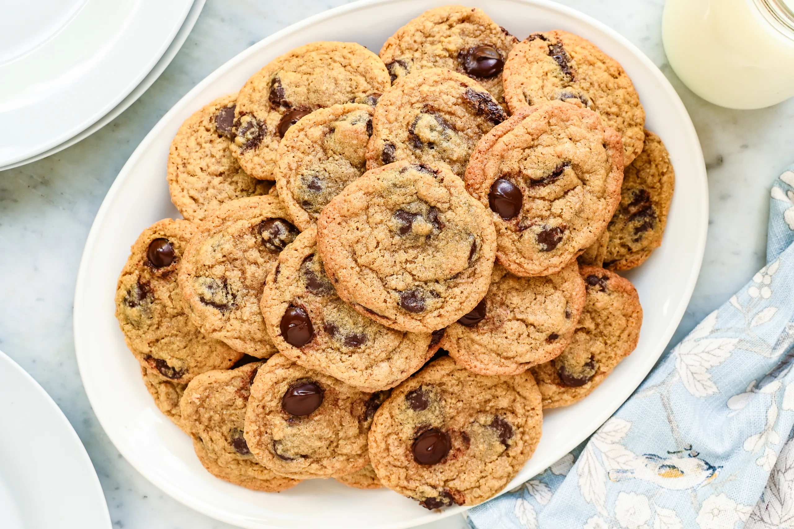 Whole wheat chocolate chip cookies piled on a white platter with milk nearby.