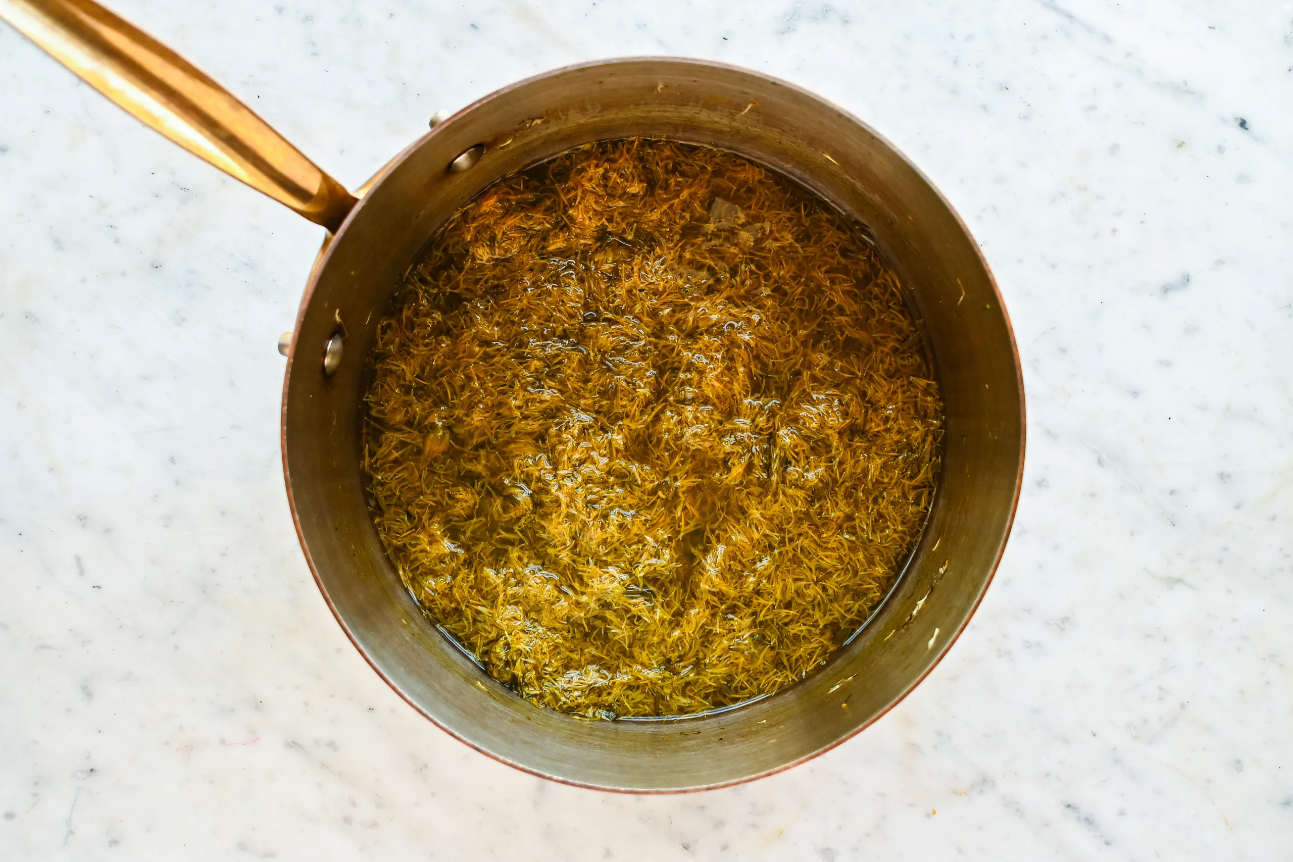 Dandelion flower tea simmering in a saucepan before being strained for homemade dandelion honey.