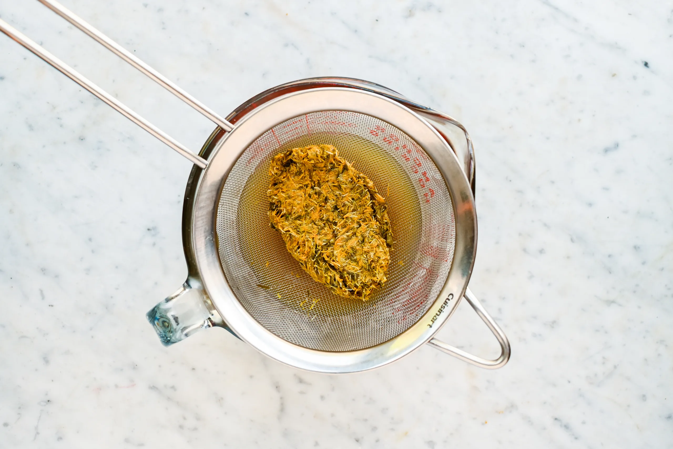 Cooked dandelion petals draining through a fine mesh strainer after simmering.