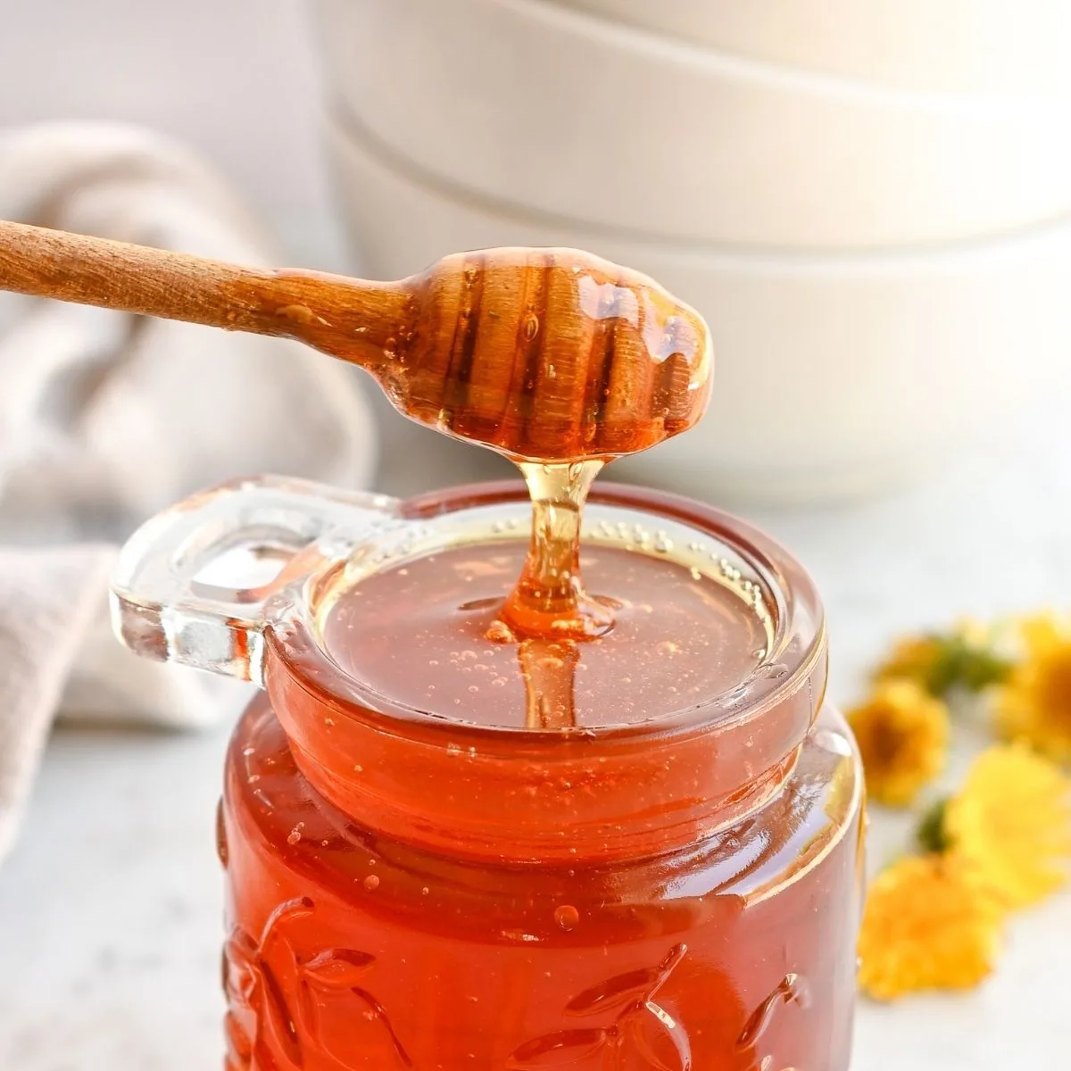 Homemade dandelion honey dripping from a wooden honey dipper into a glass jar.