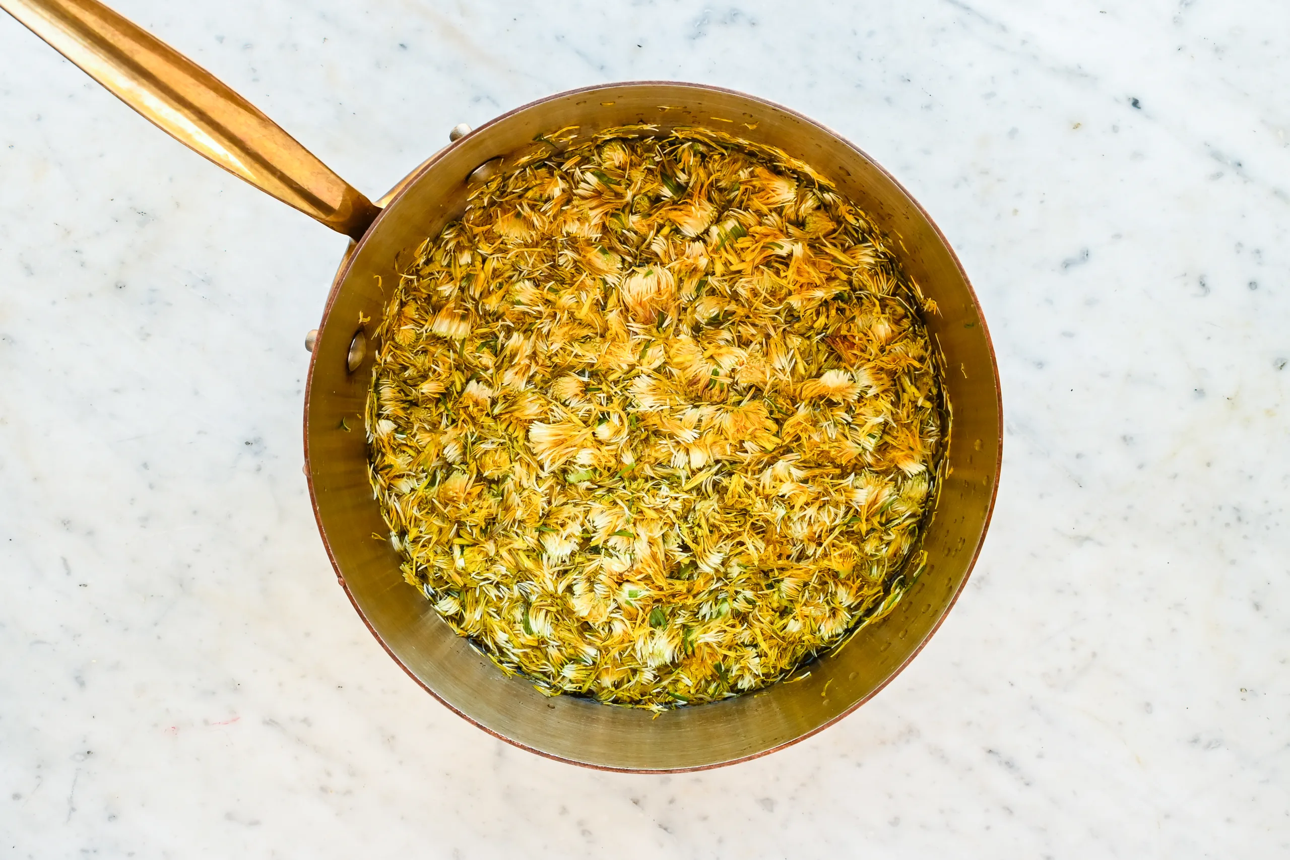 Dandelion petals steeping in water in a saucepan to make dandelion honey.
