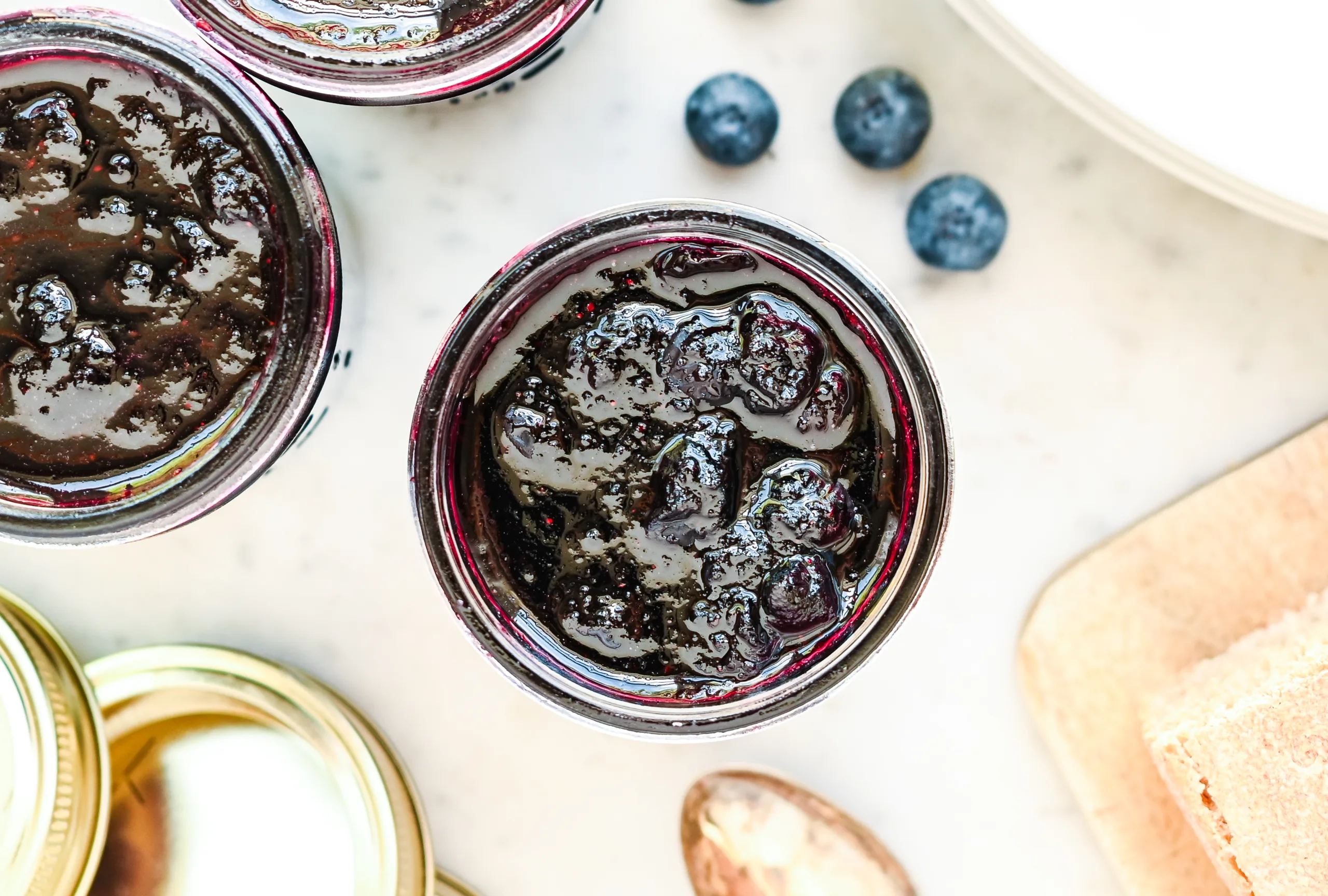 Overhead close up of thick homemade blueberry preserves inside a mason jar, with whole blueberries visible throughout the glossy jam.