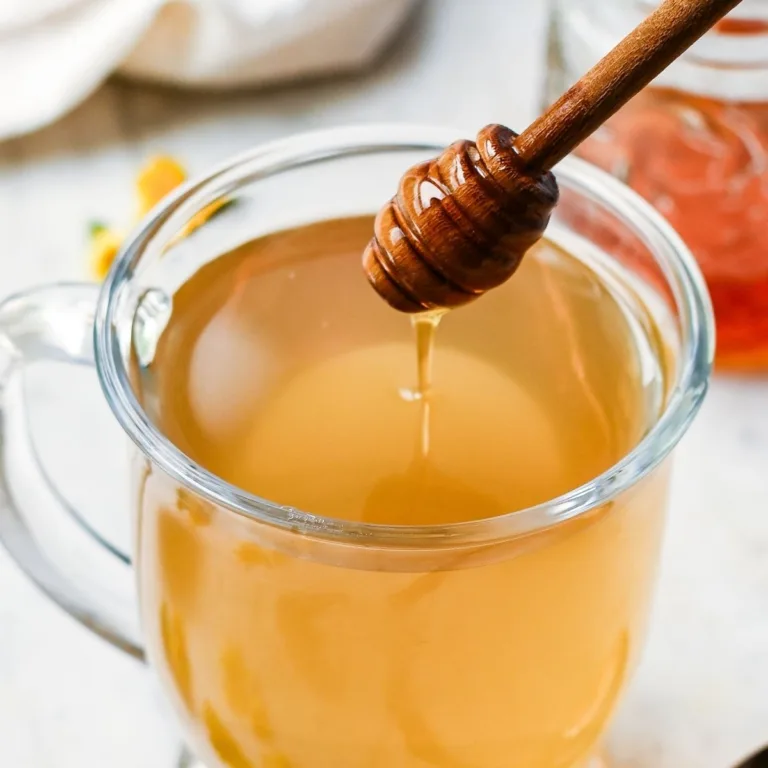 Glass mug of roasted dandelion root tea with honey being drizzled in from a wooden honey dipper.