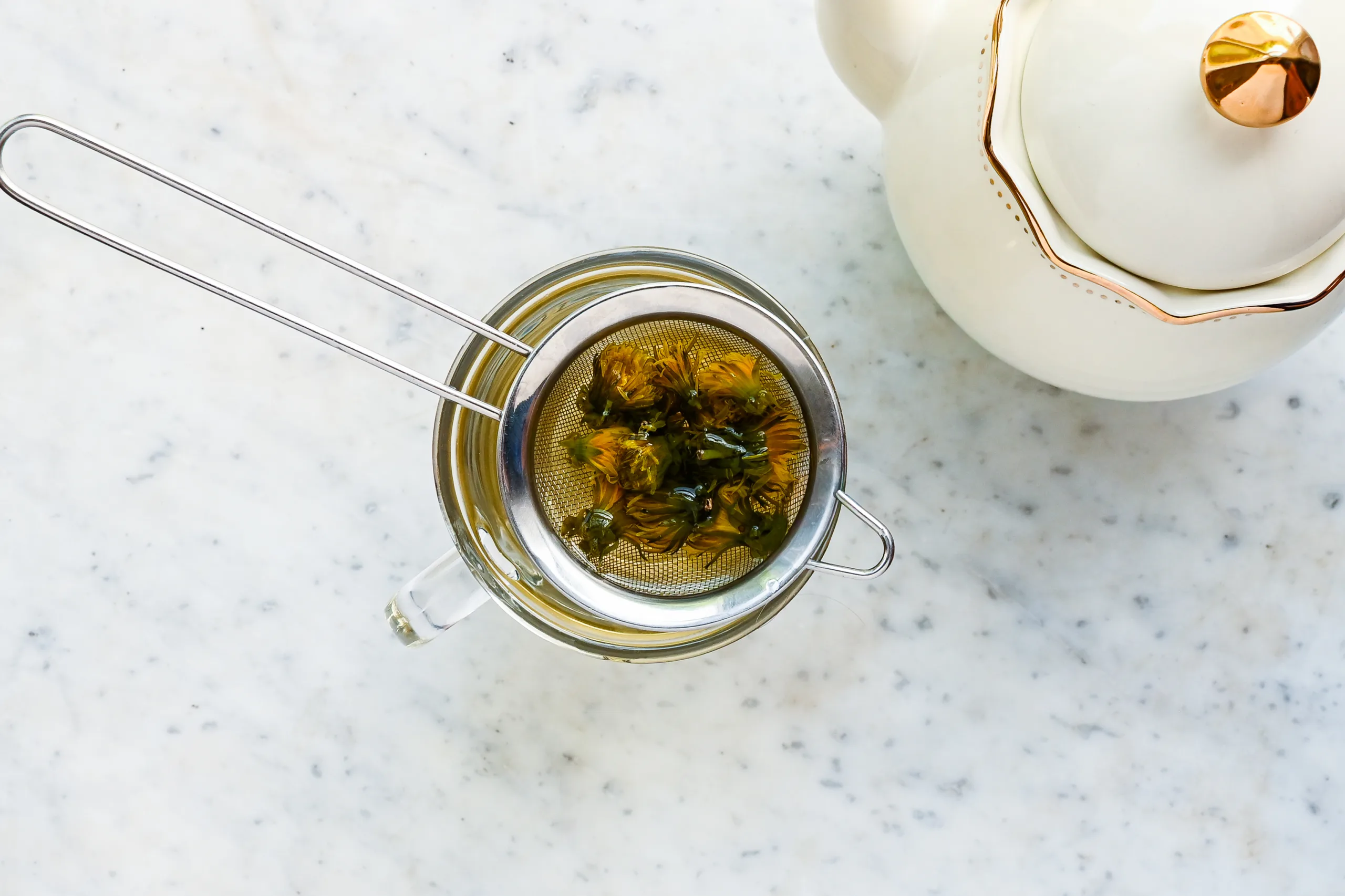 Fresh dandelion flower tea being strained into a glass mug after steeping.