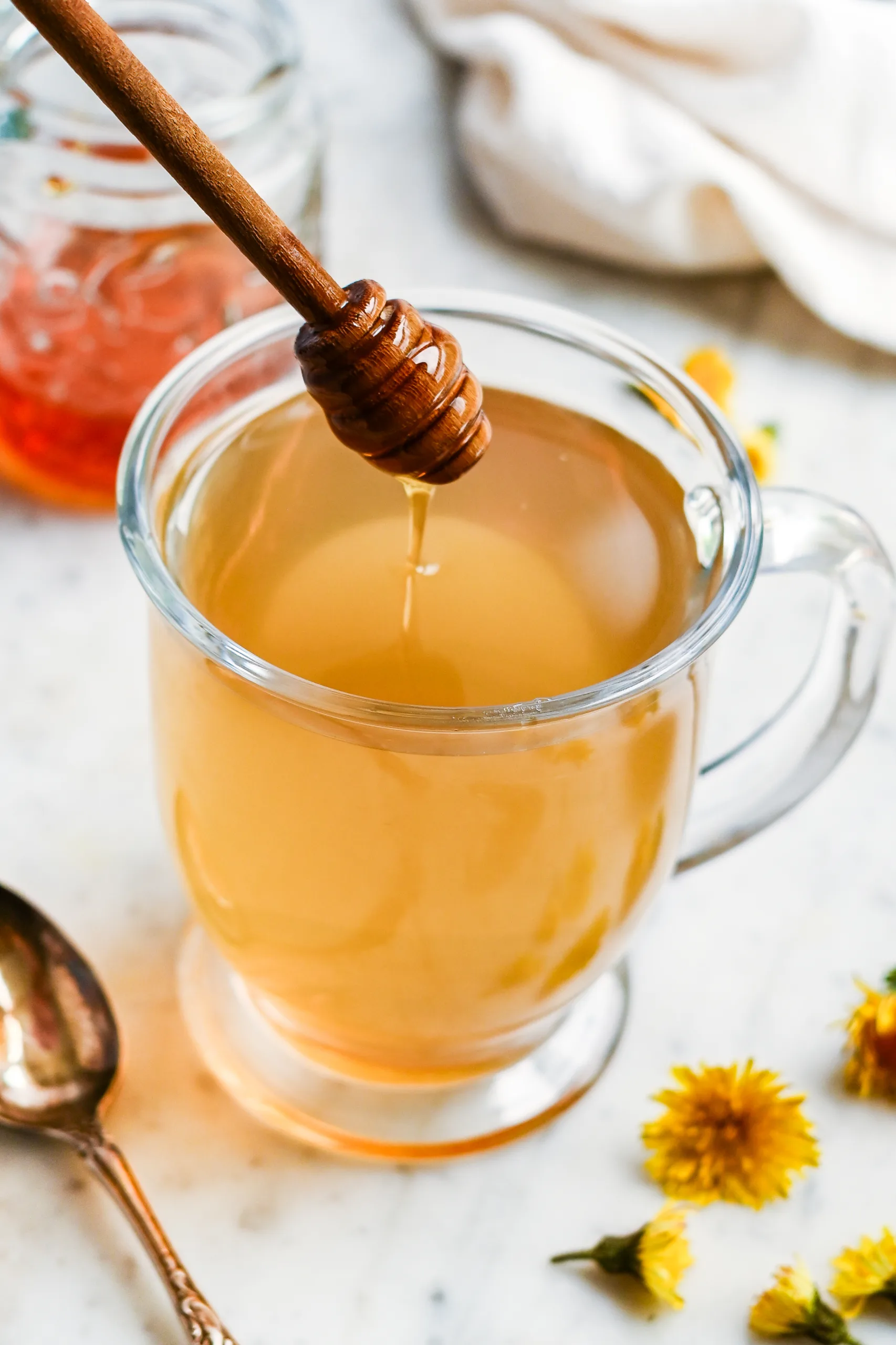 Warm dandelion flower tea sweetened with honey in a clear glass mug.