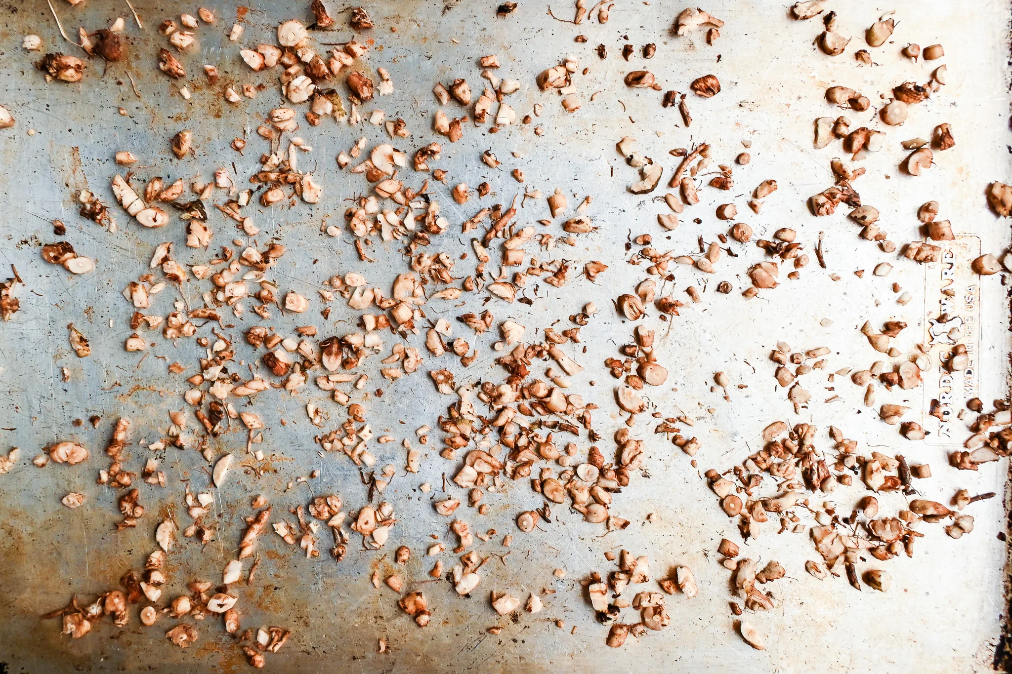 Chopped dandelion roots spread on a baking sheet before roasting for dandelion root tea.