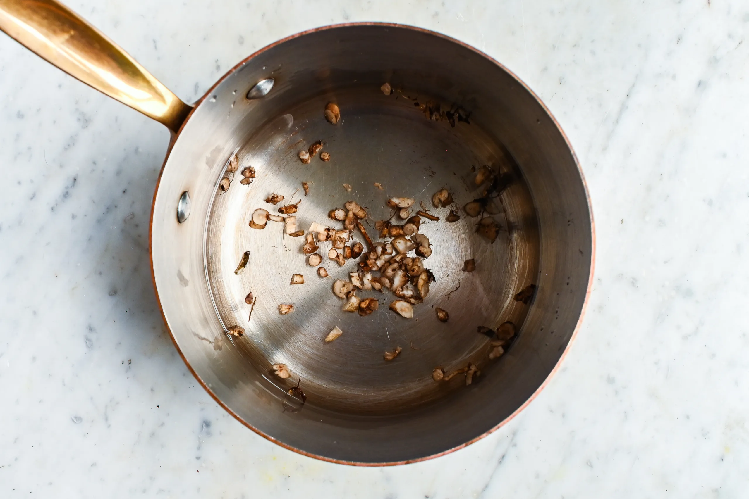 Chopped roasted dandelion roots in a copper saucepan for making roasted dandelion root tea.
