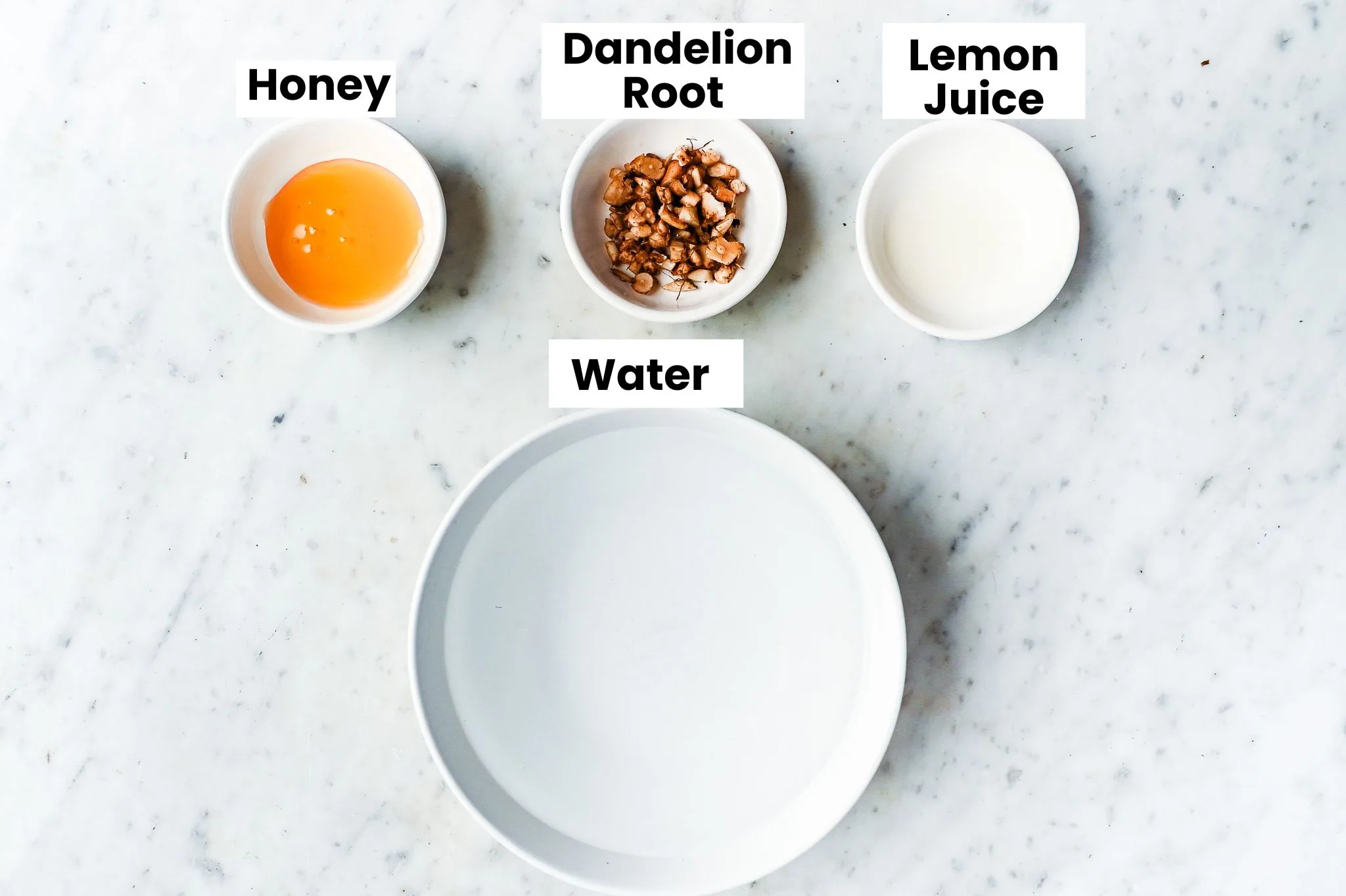Ingredients for roasted dandelion root tea with dried dandelion roots, water, honey, and milk on a marble counter.