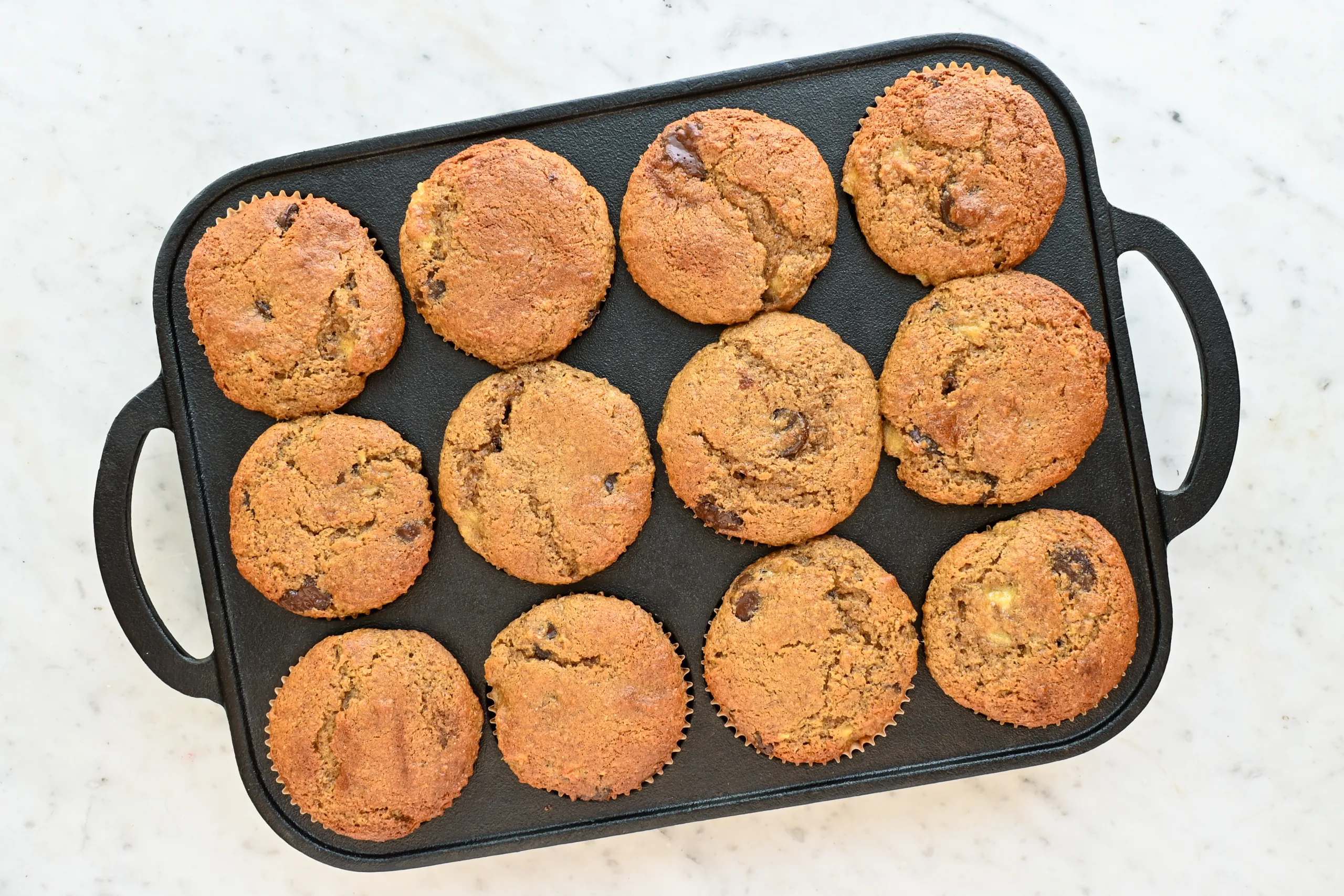 Baked whole wheat banana muffins with chocolate chips cooling in a black muffin pan.