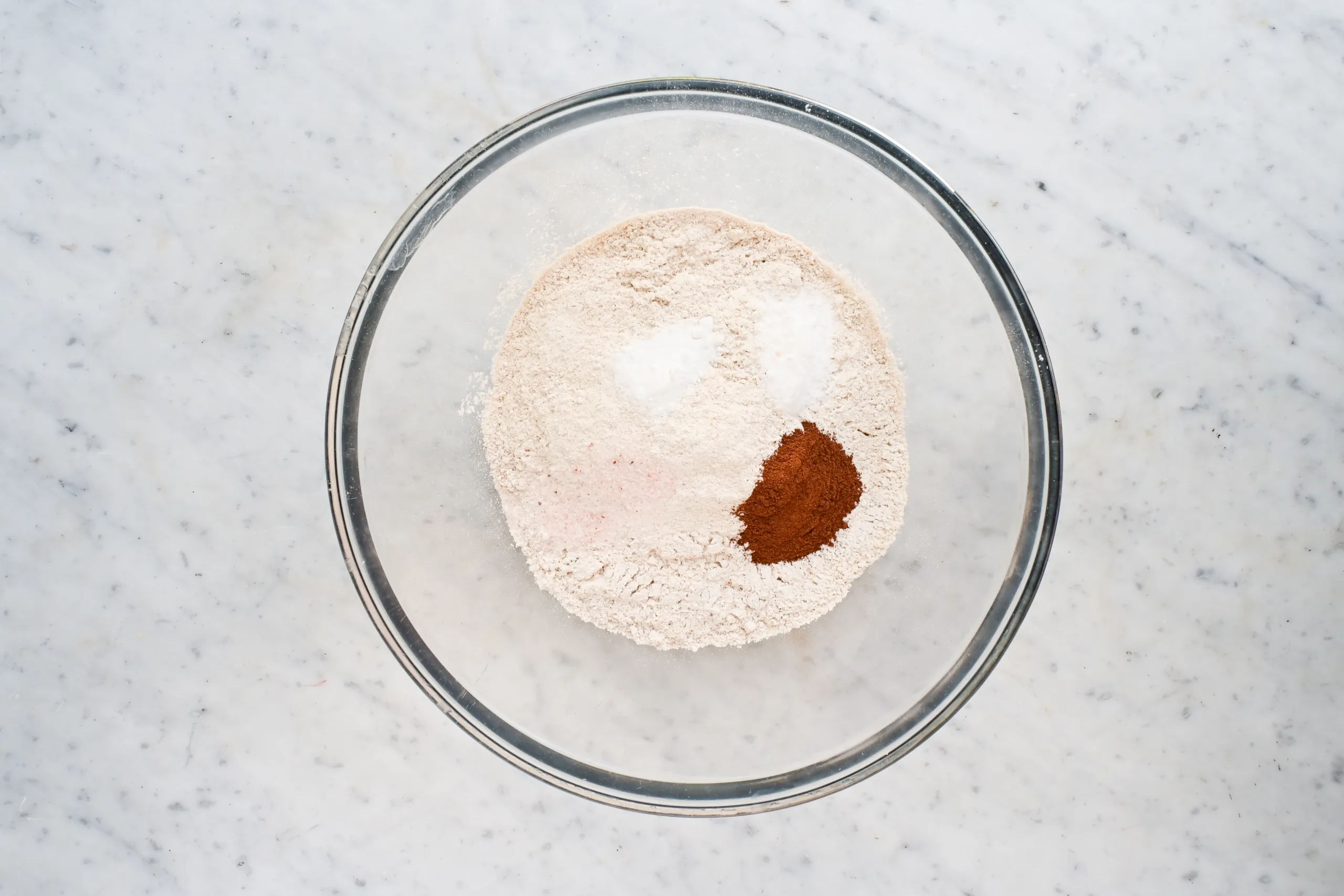 Fresh milled wheat flour, baking soda, baking powder, salt, and cinnamon in a glass mixing bowl.
